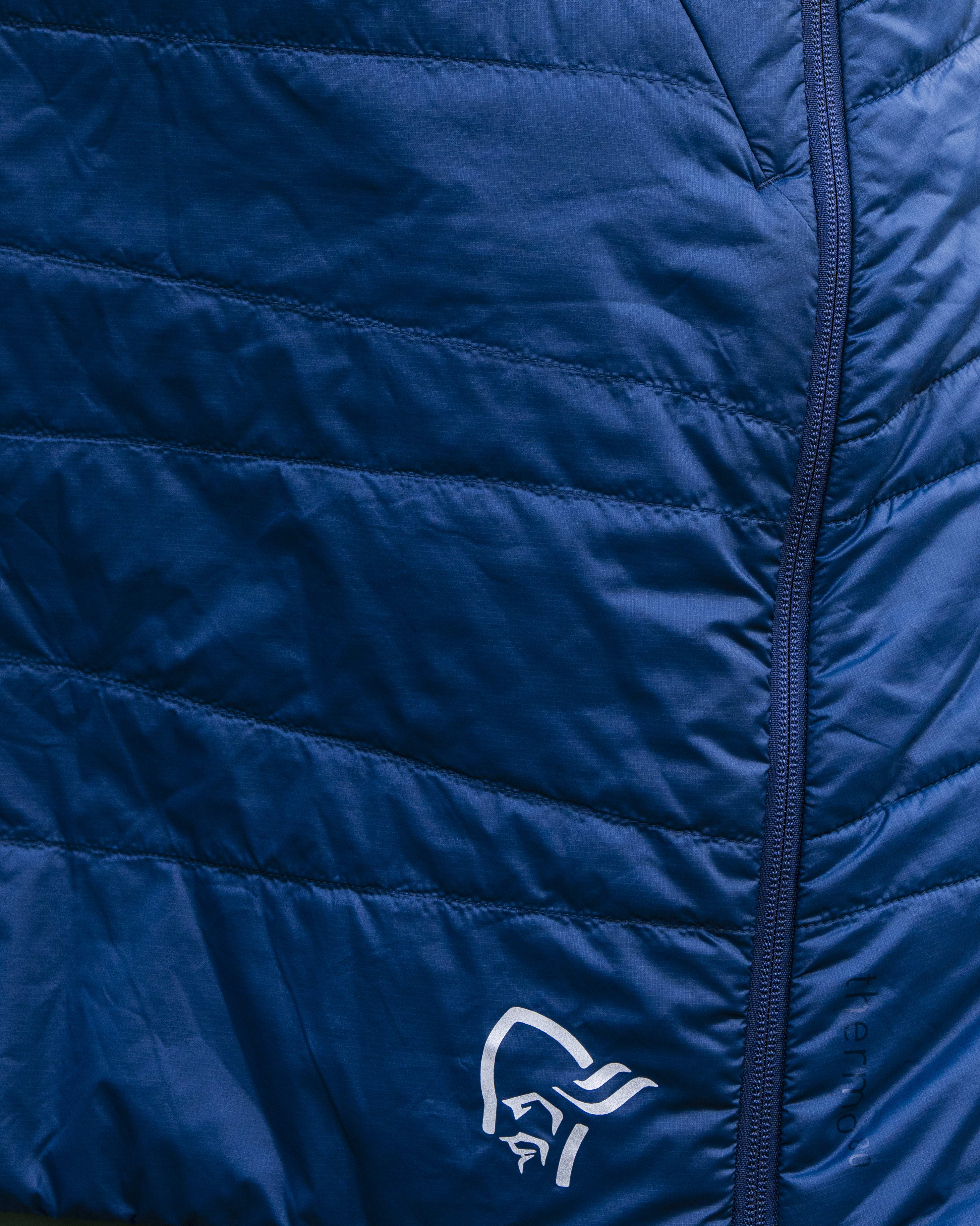 A woman is wearing a blue Norrøna insulated skirt.  The skirt has a zipper on the side and a white logo.