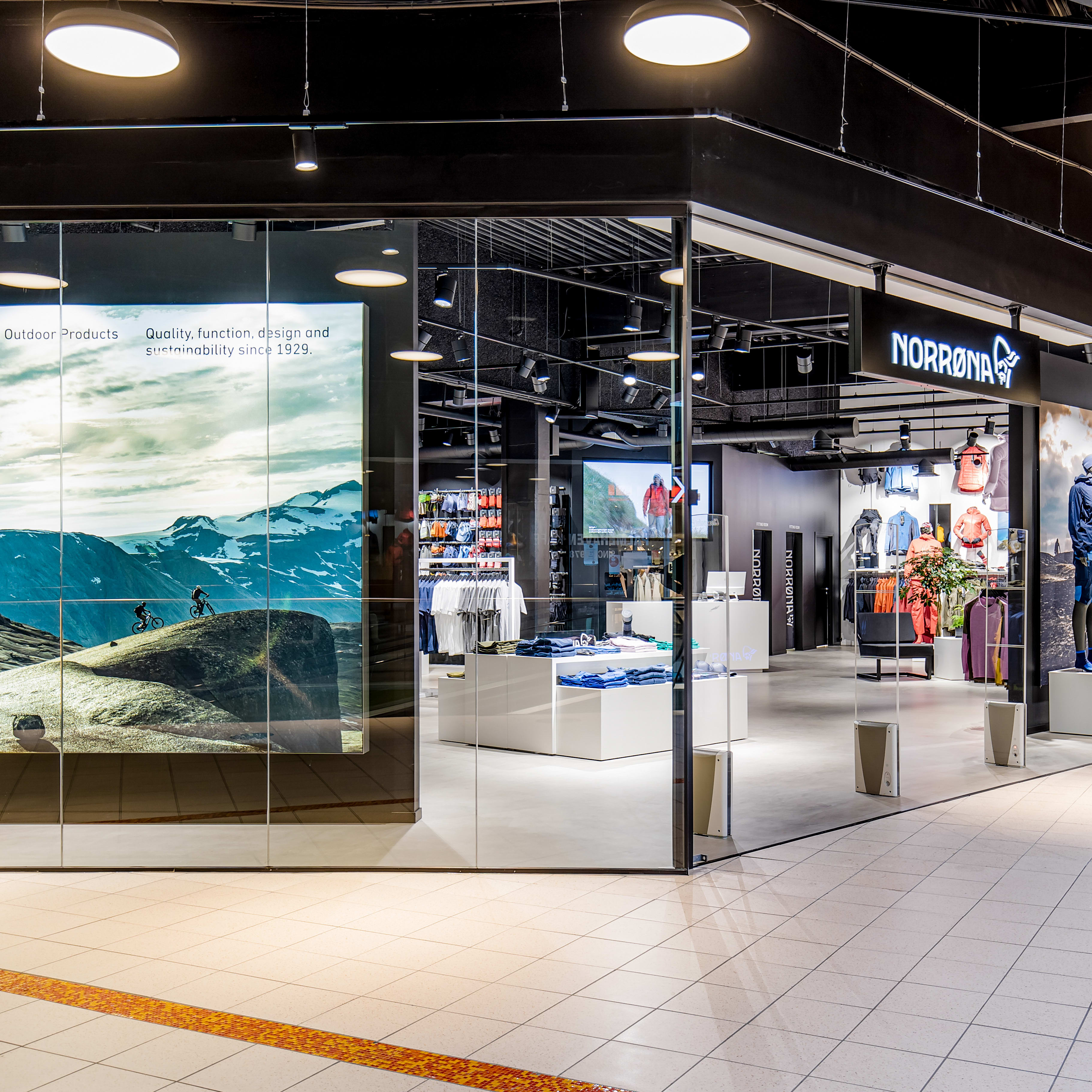 Modern glass storefront of a Norrøna retail store displaying outdoor clothing on mannequins.