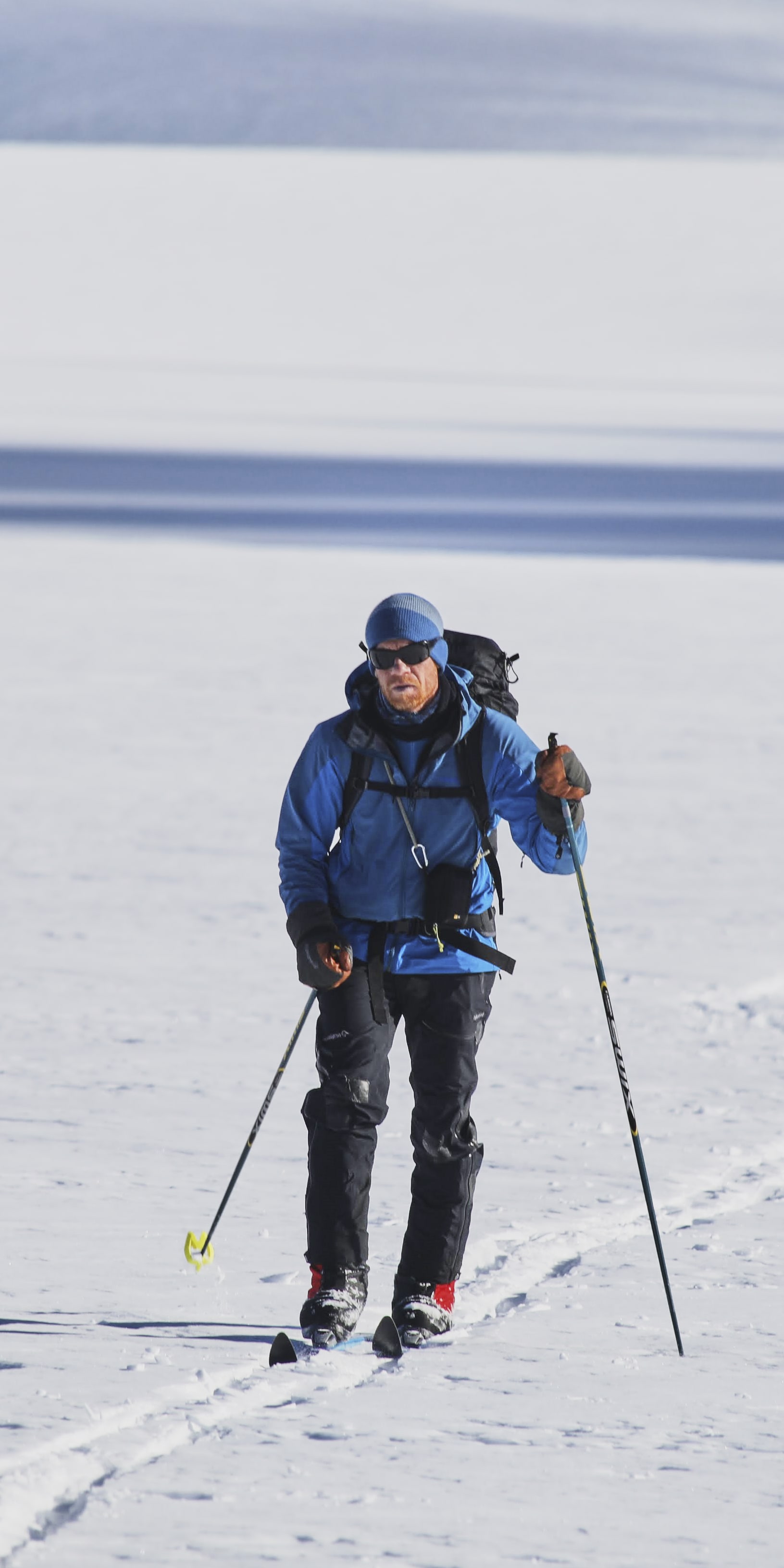 A person wearing Norrøna clothing backcountry skis on a snowy landscape.  
