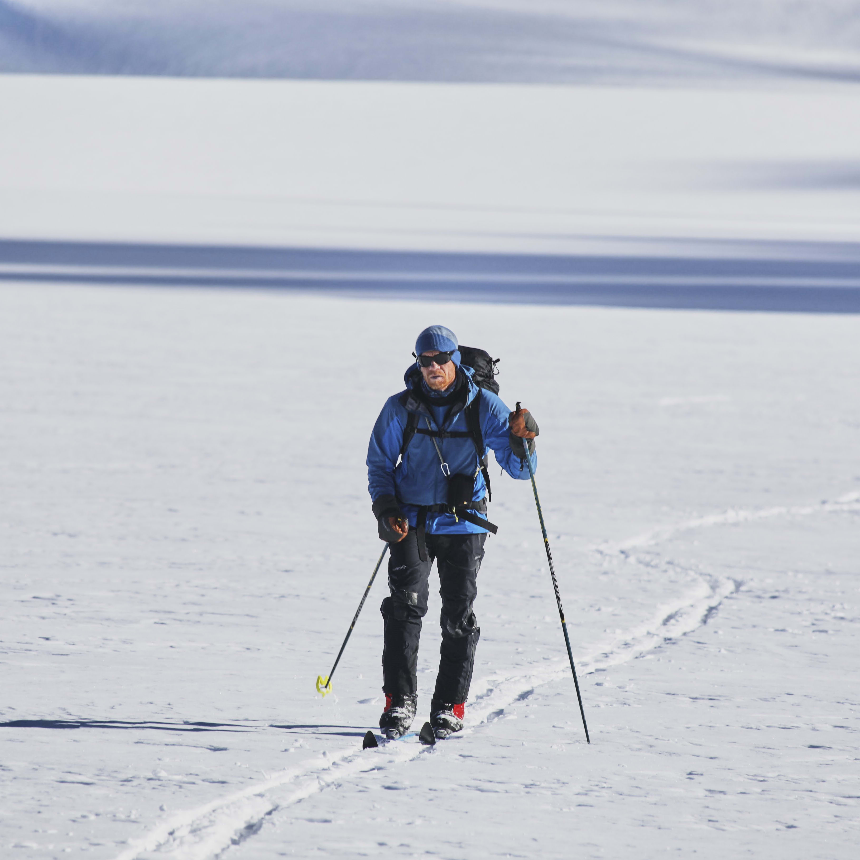A person wearing Norrøna clothing backcountry skis on a snowy landscape.  
