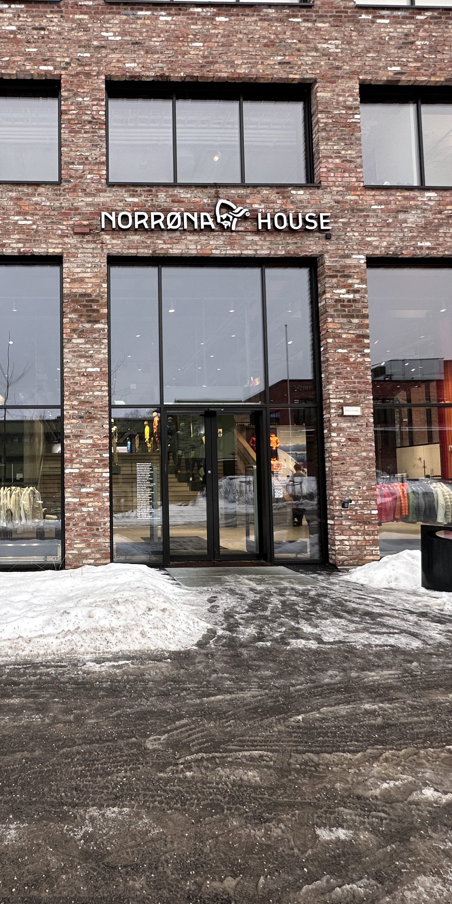 "Exterior of Norrøna House store in winter. Brick building with large windows displaying Norrøna apparel. Signage is visible."