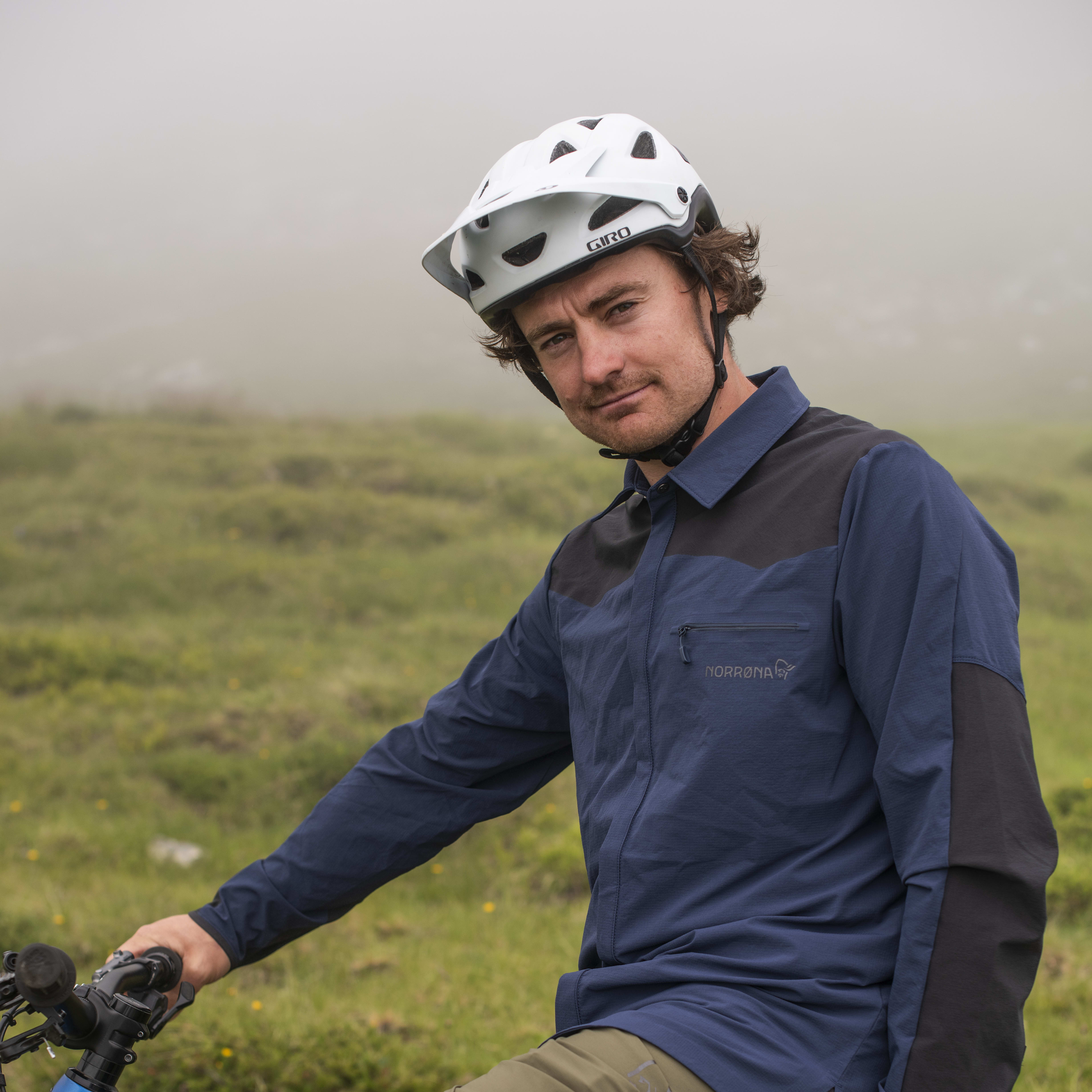 A man wearing a Norrøna shirt and helmet is sitting on a blue Trek mountain bike.