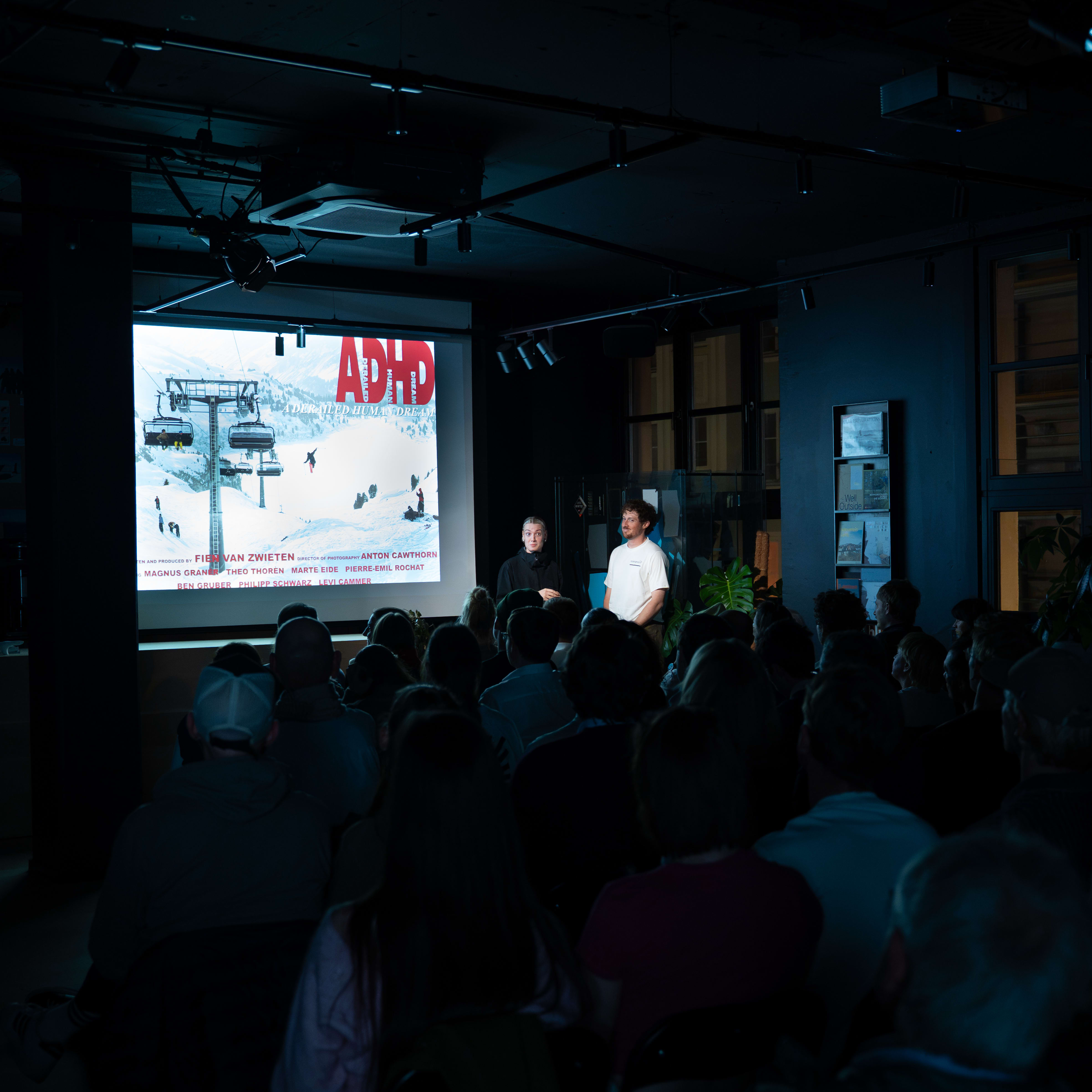 Presenters in Norrøna clothing stand by a screen showing 'ADHD' before a seated audience in a dark venue.