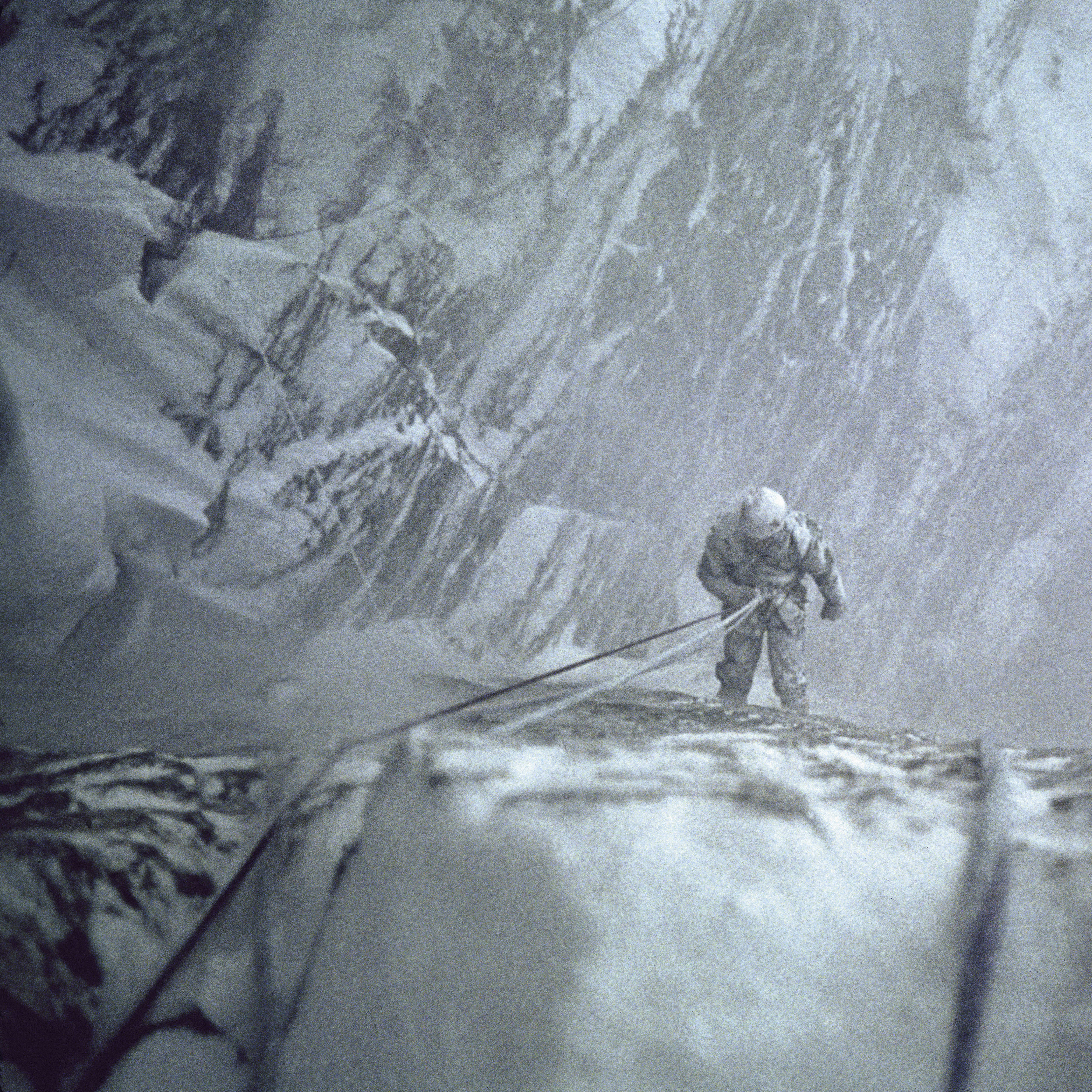 A person rappelling down a snowy mountainside.  The person is wearing a helmet and is attached to a rope.  The mountain is covered in snow and ice.