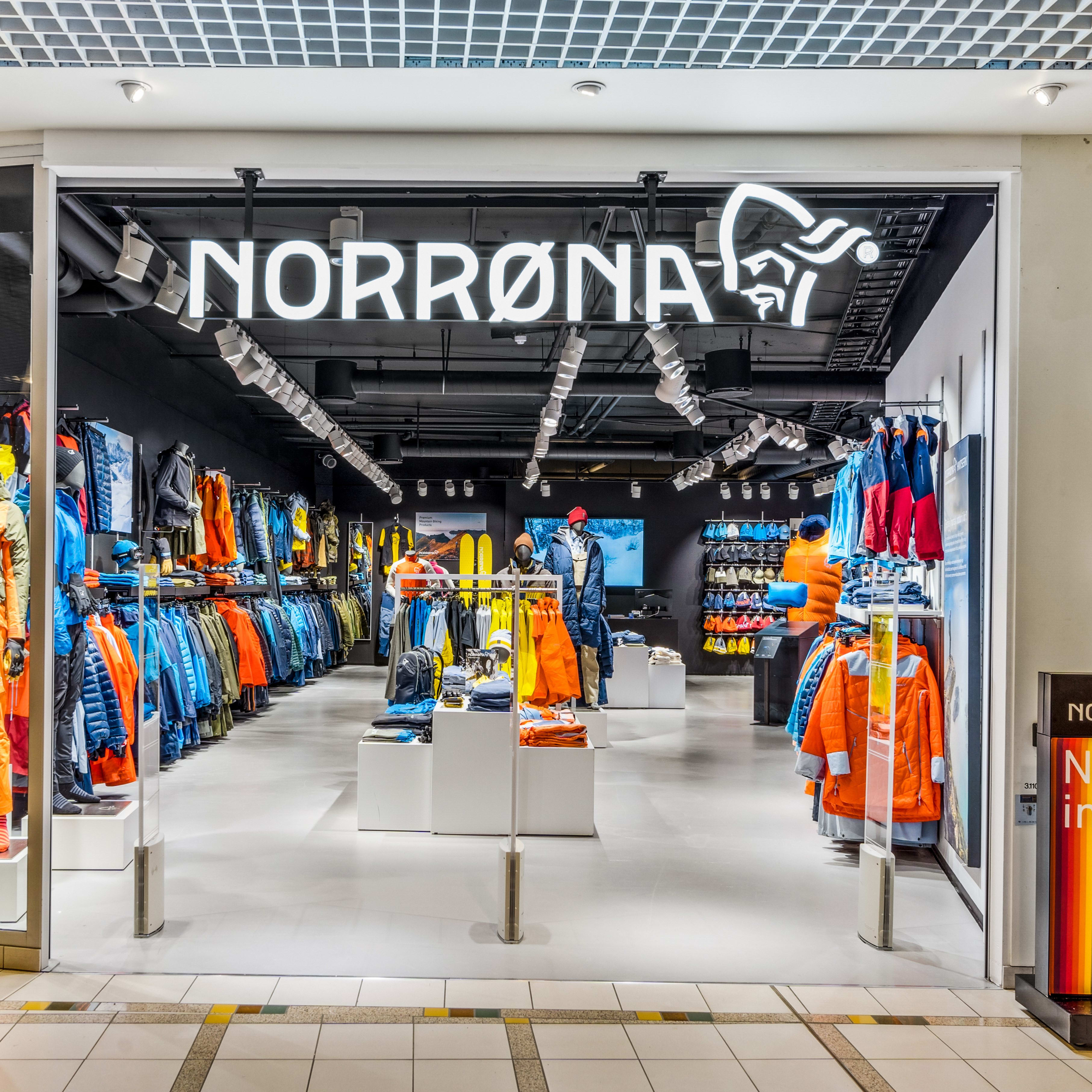 A Norrøna store storefront with mannequins wearing orange and blue outdoor clothing. The store is well-lit and has a white tiled floor.  
