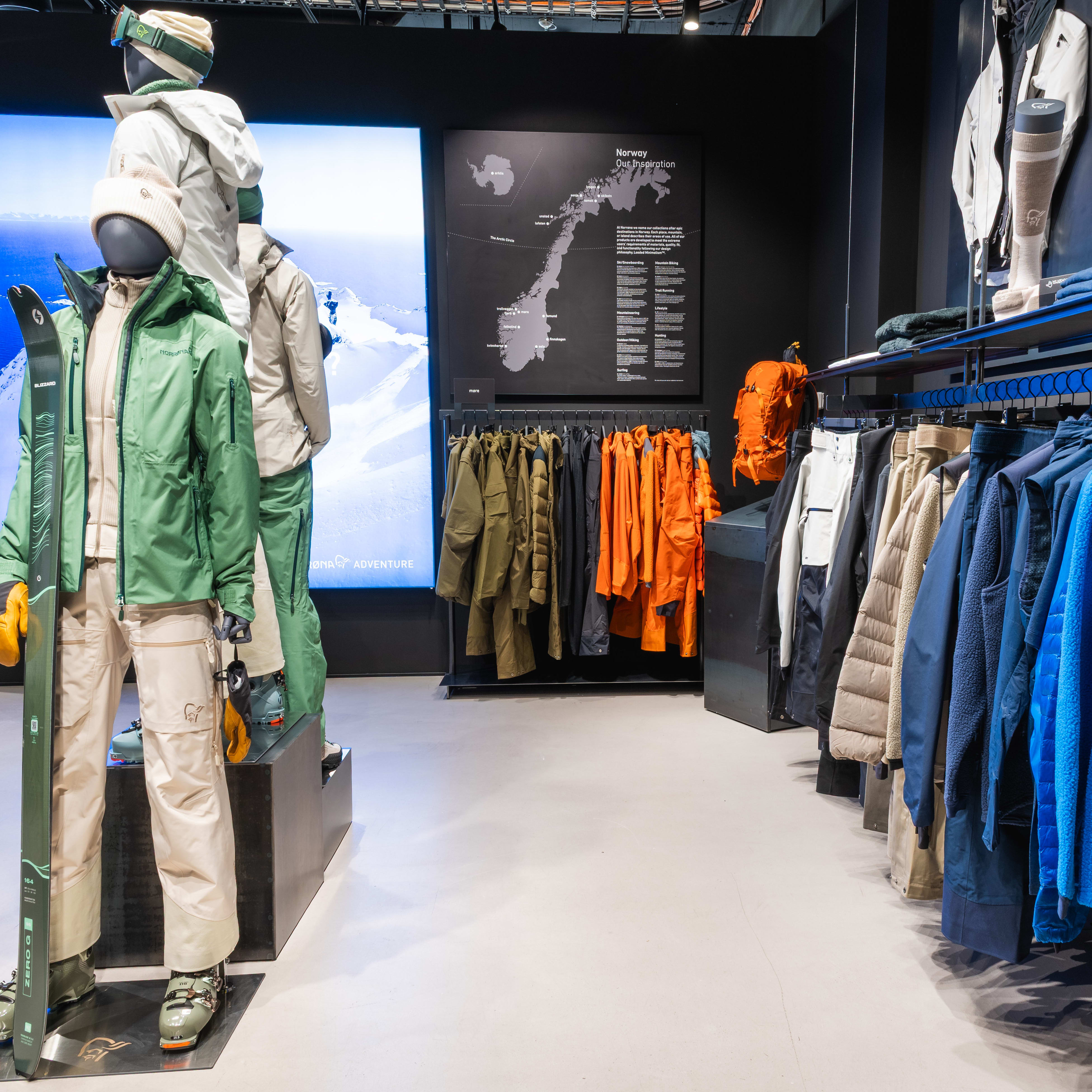 A retail store interior displays a range of Norrøna outdoor apparel on mannequins and racks, featuring colorful jackets, pants, and a ski.