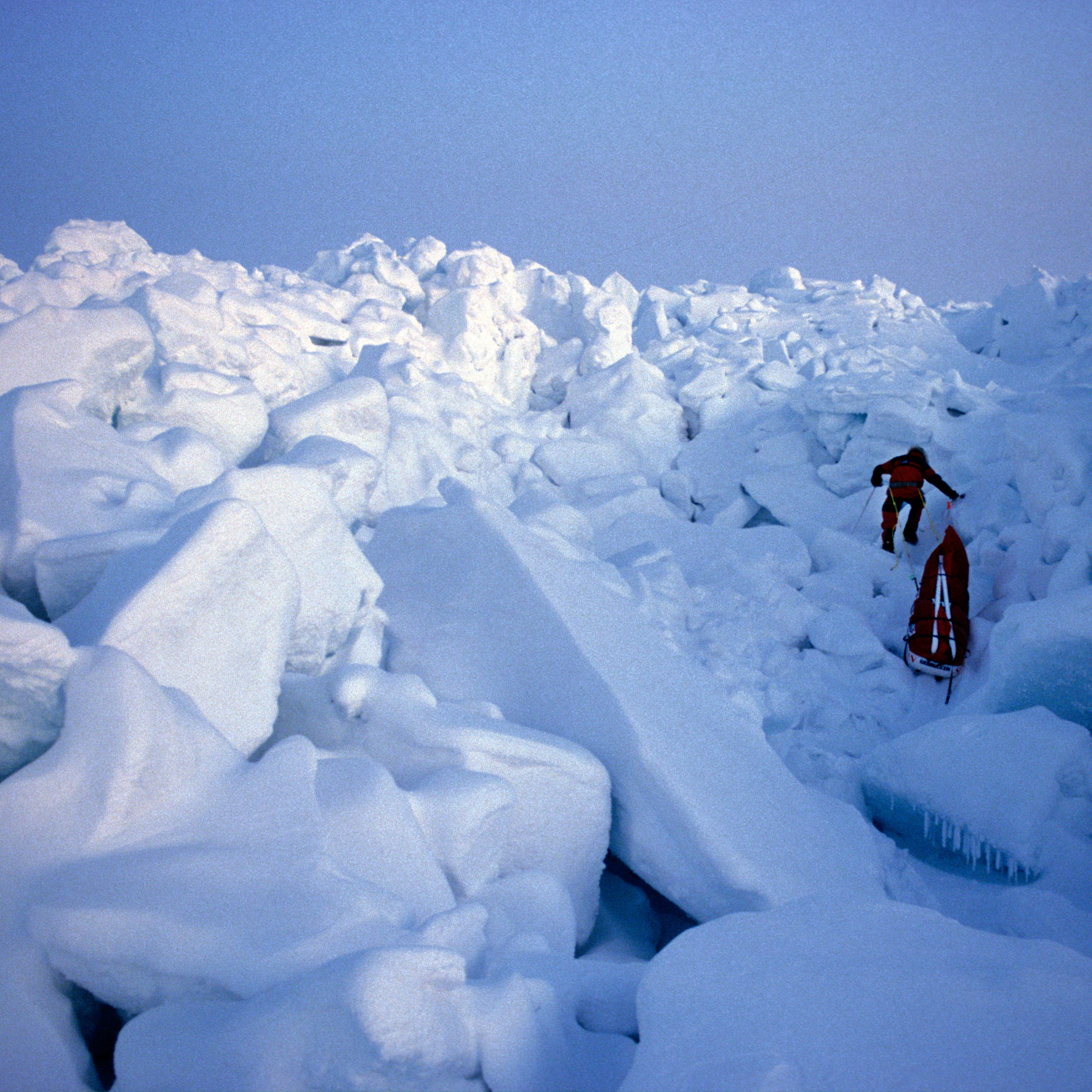 A person in red clothing pulls a Norrøna sled over a snowy, icy landscape. 

