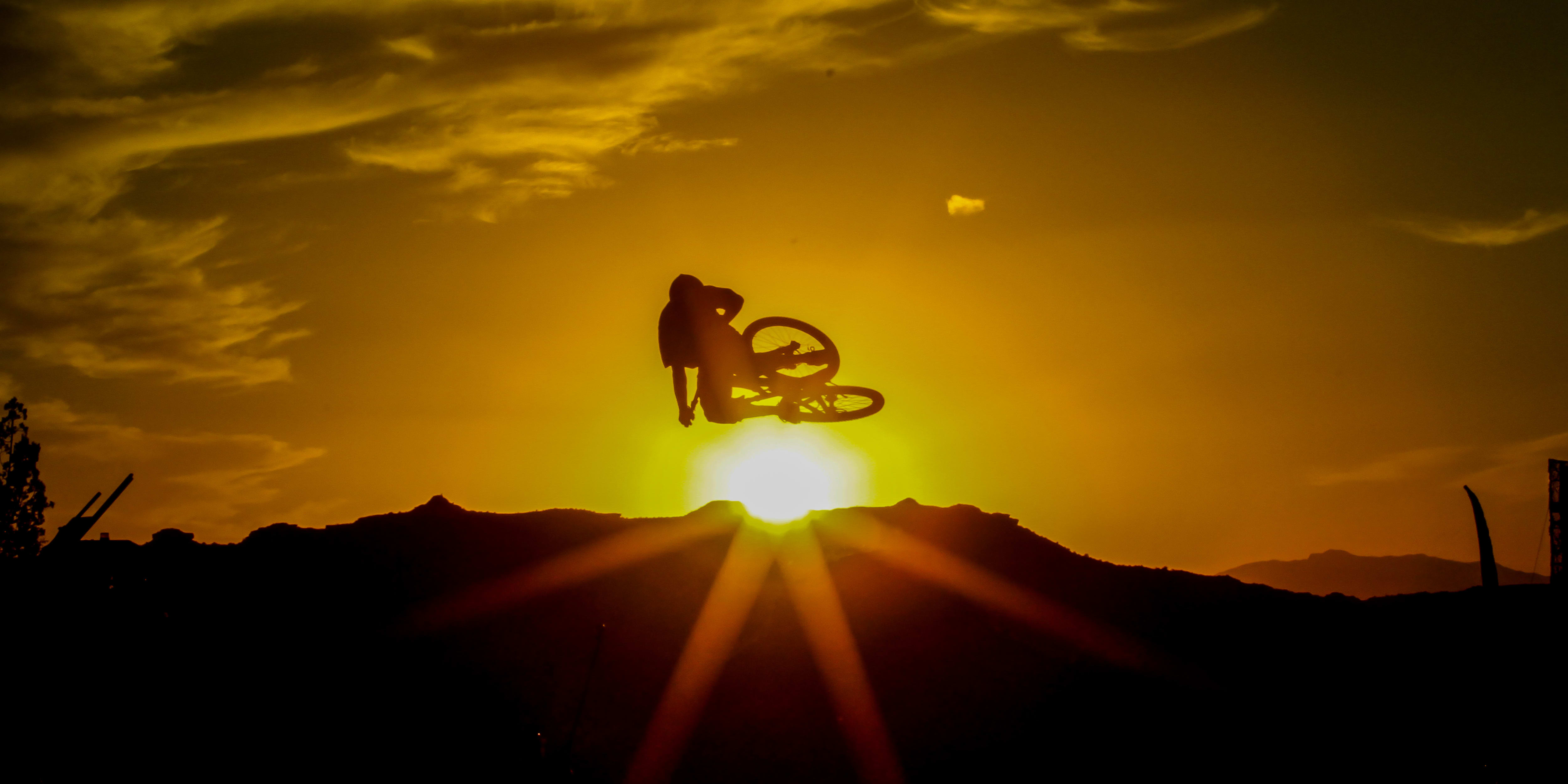 Silhouette of a biker in Norrøna gear mid-air with a sunset background.
