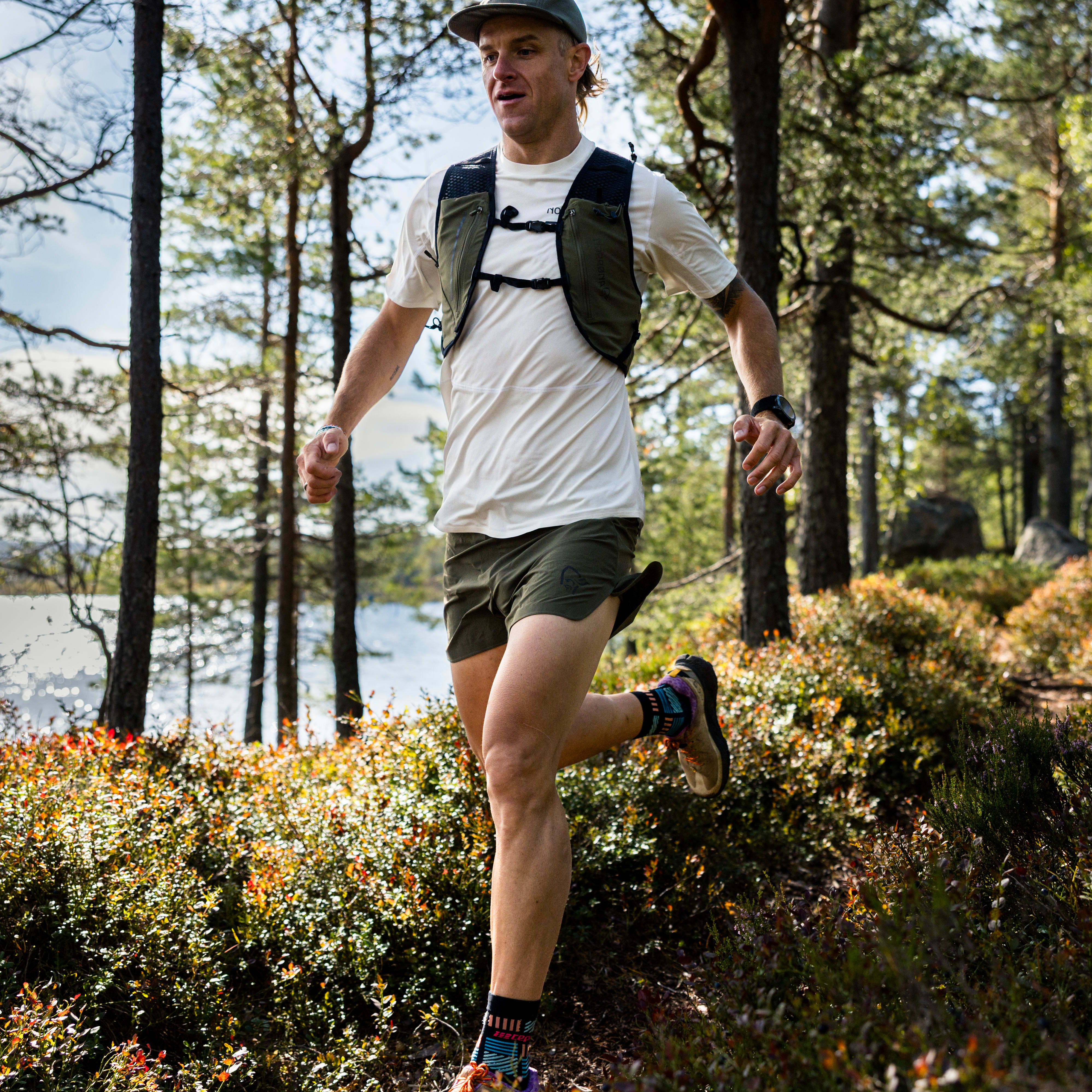 A man trail running through a forest. He is wearing a Norrøna vest and shorts.