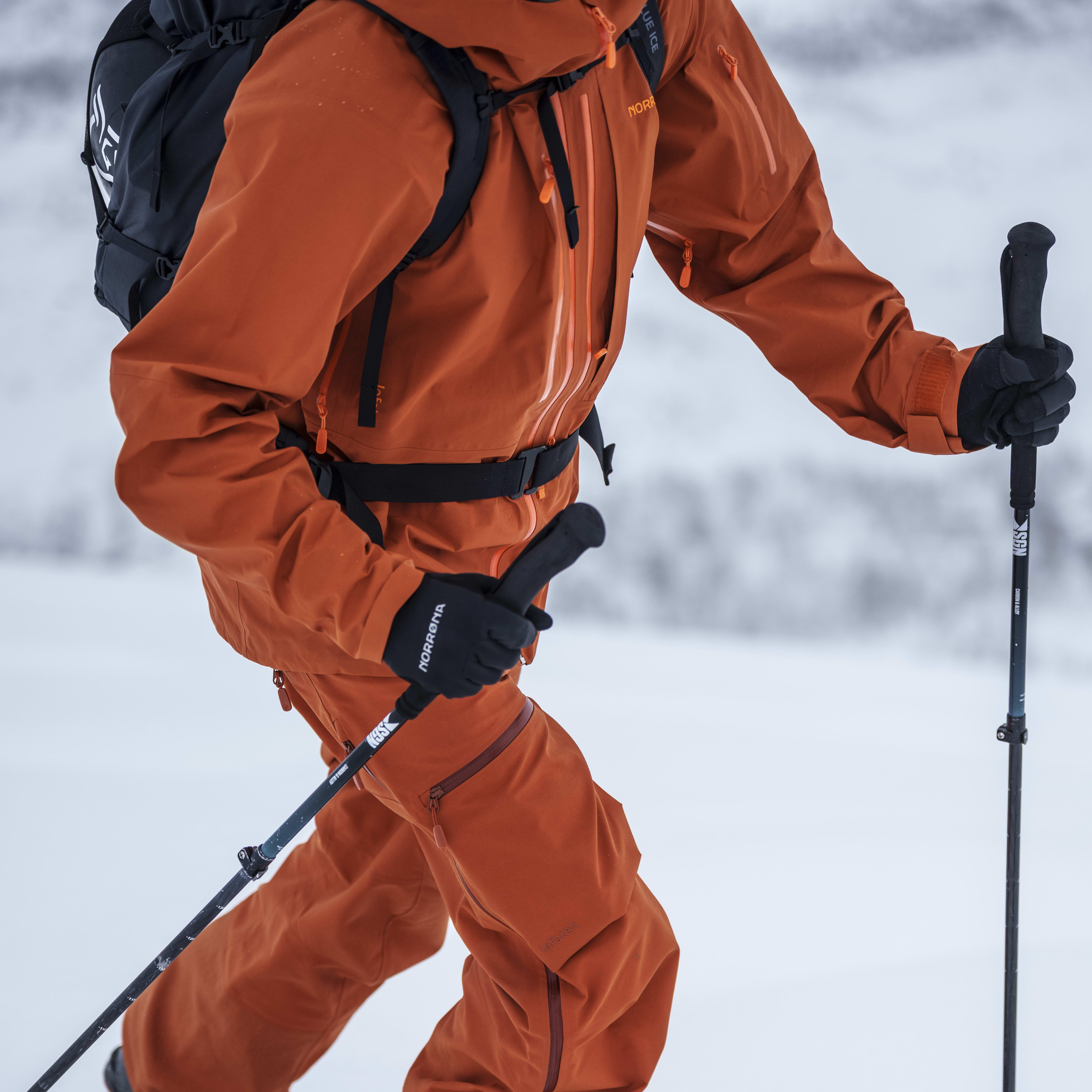 A person wearing a Norrøna jacket and pants skis down a snowy slope. 

