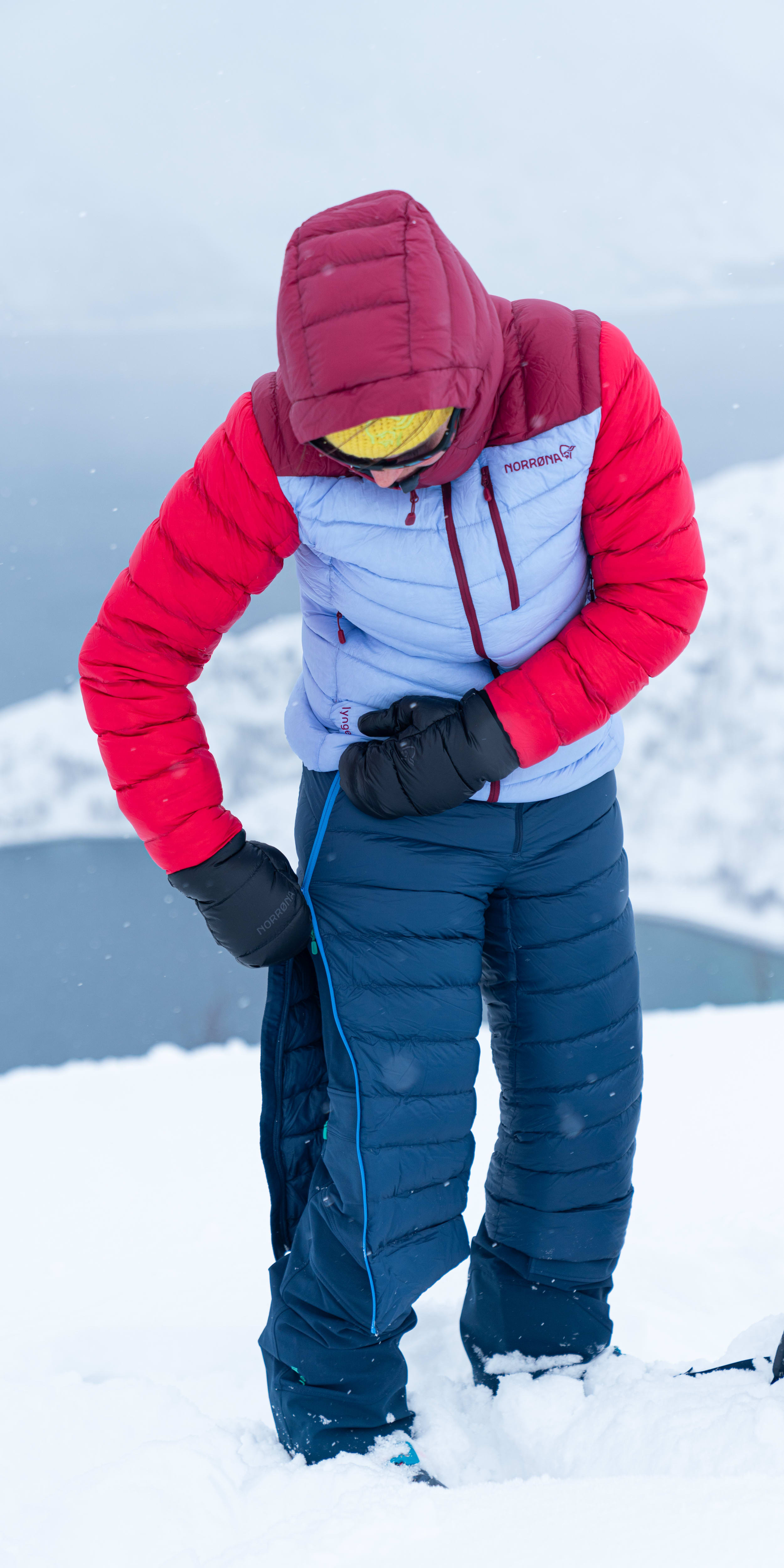 A person wearing a red and blue Norrøna jacket and pants stands in snow.