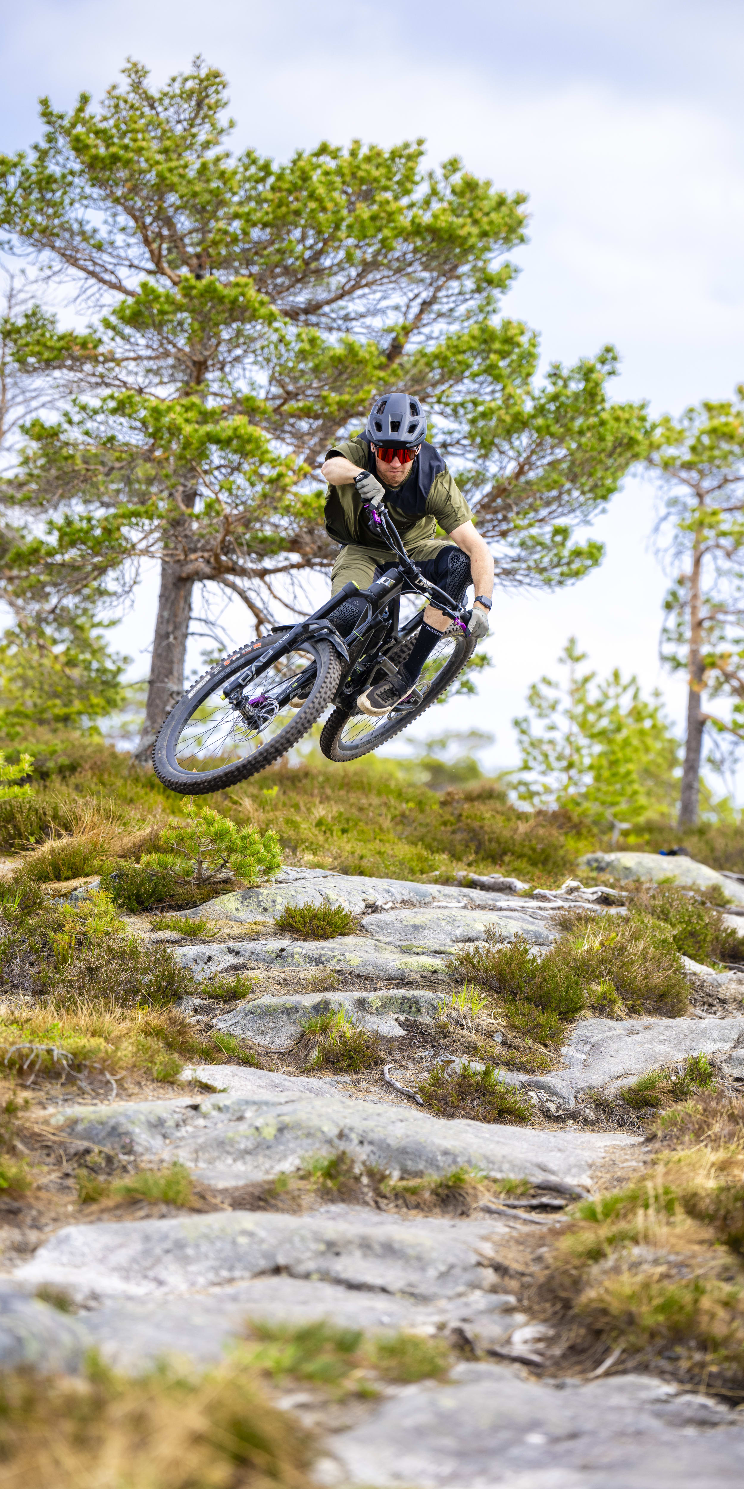 A person wearing a Norrøna shirt and a helmet is mountain biking on a rocky trail. 
