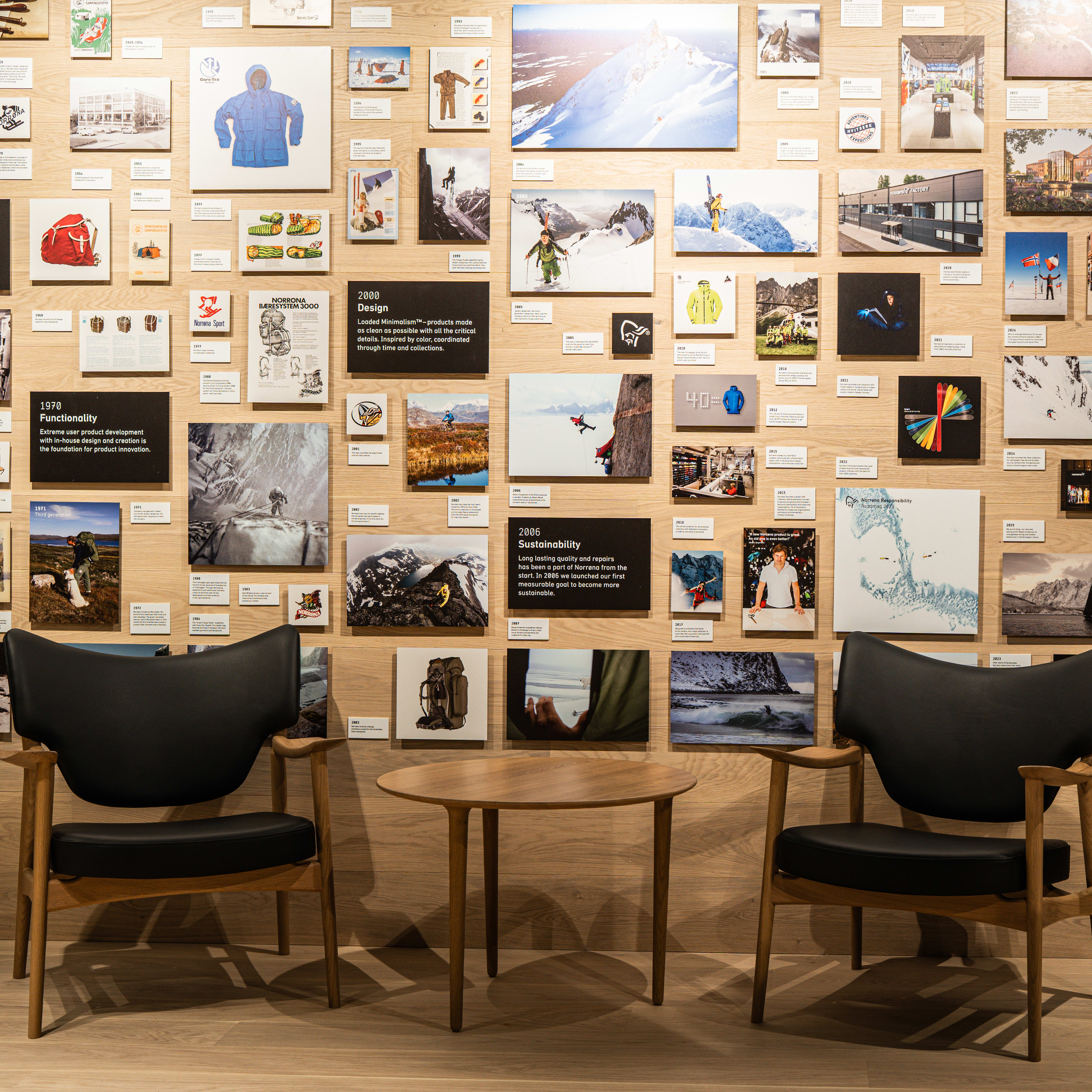 Display of Norrøna's history with photos & text panels on wood wall. Foreground: chairs and a table with a wooden finish.