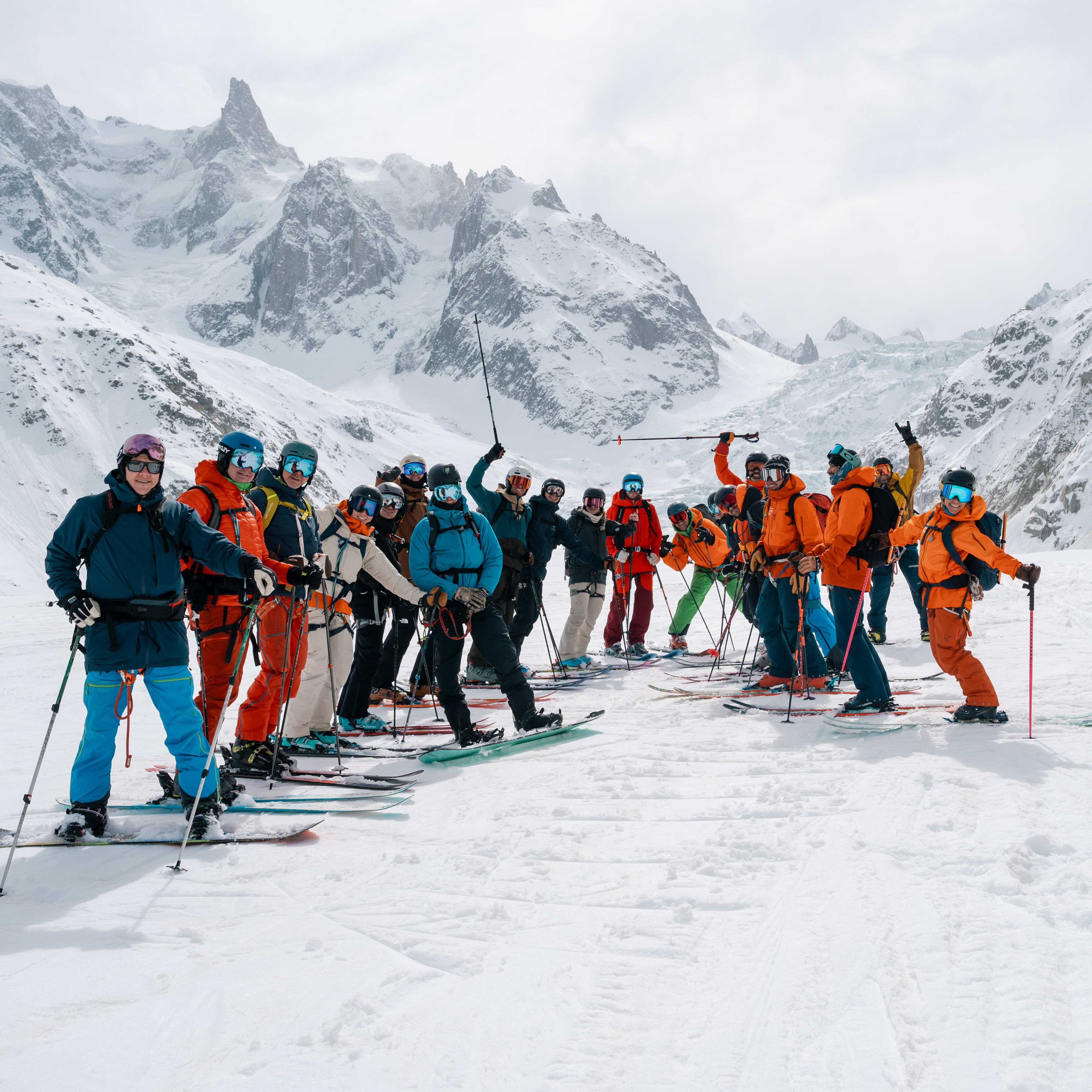 A group of skiers wearing Norrøna outerwear pose on snow with mountain peaks in the background on a cloudy day.
