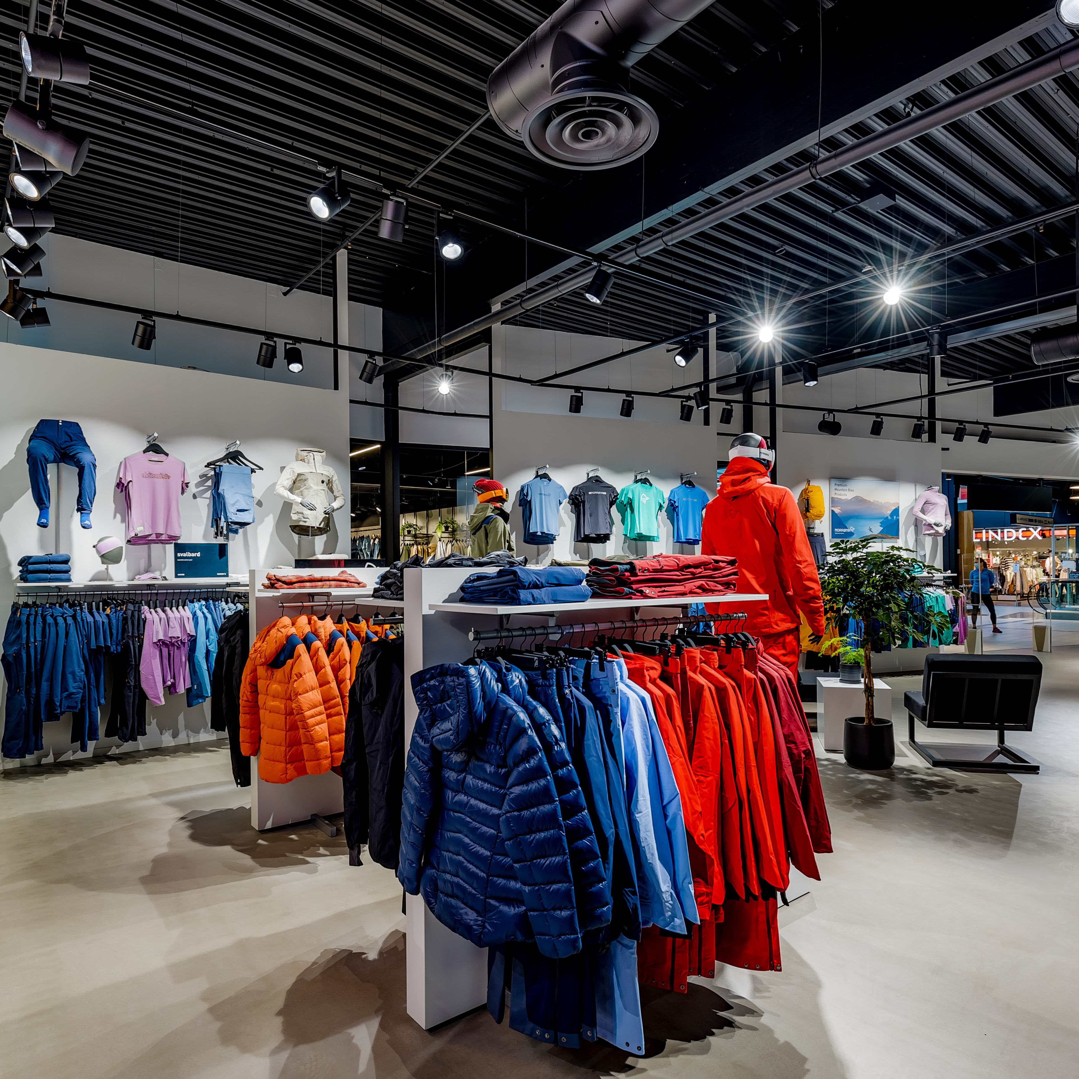Brightly lit retail store displaying colorful Norrøna outdoor apparel on racks and mannequins.