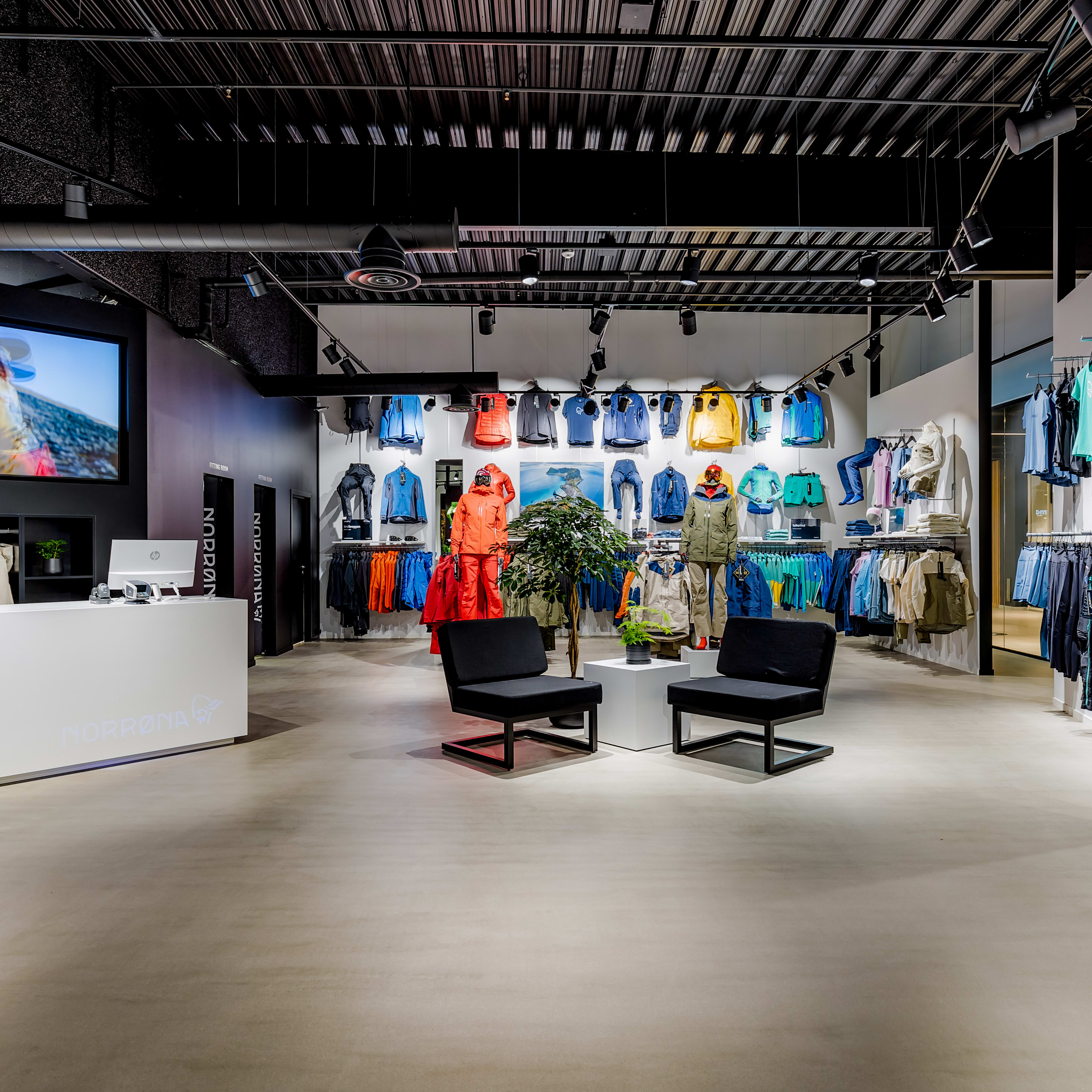 Norrøna retail store interior showing colorful outdoor clothing on display, a service counter, and a seating area.