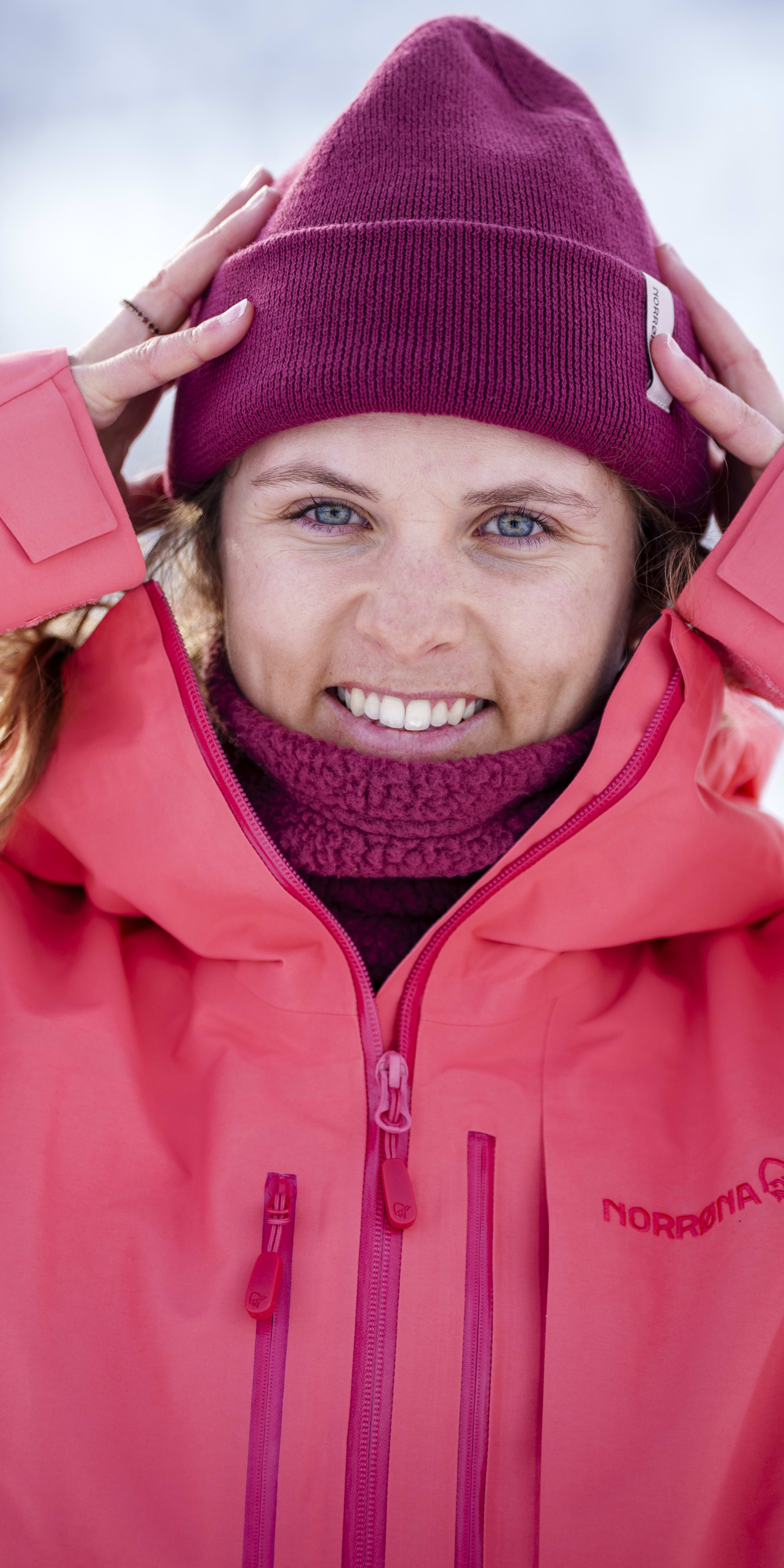 Smiling woman wearing a pink Norrøna jacket and beanie.