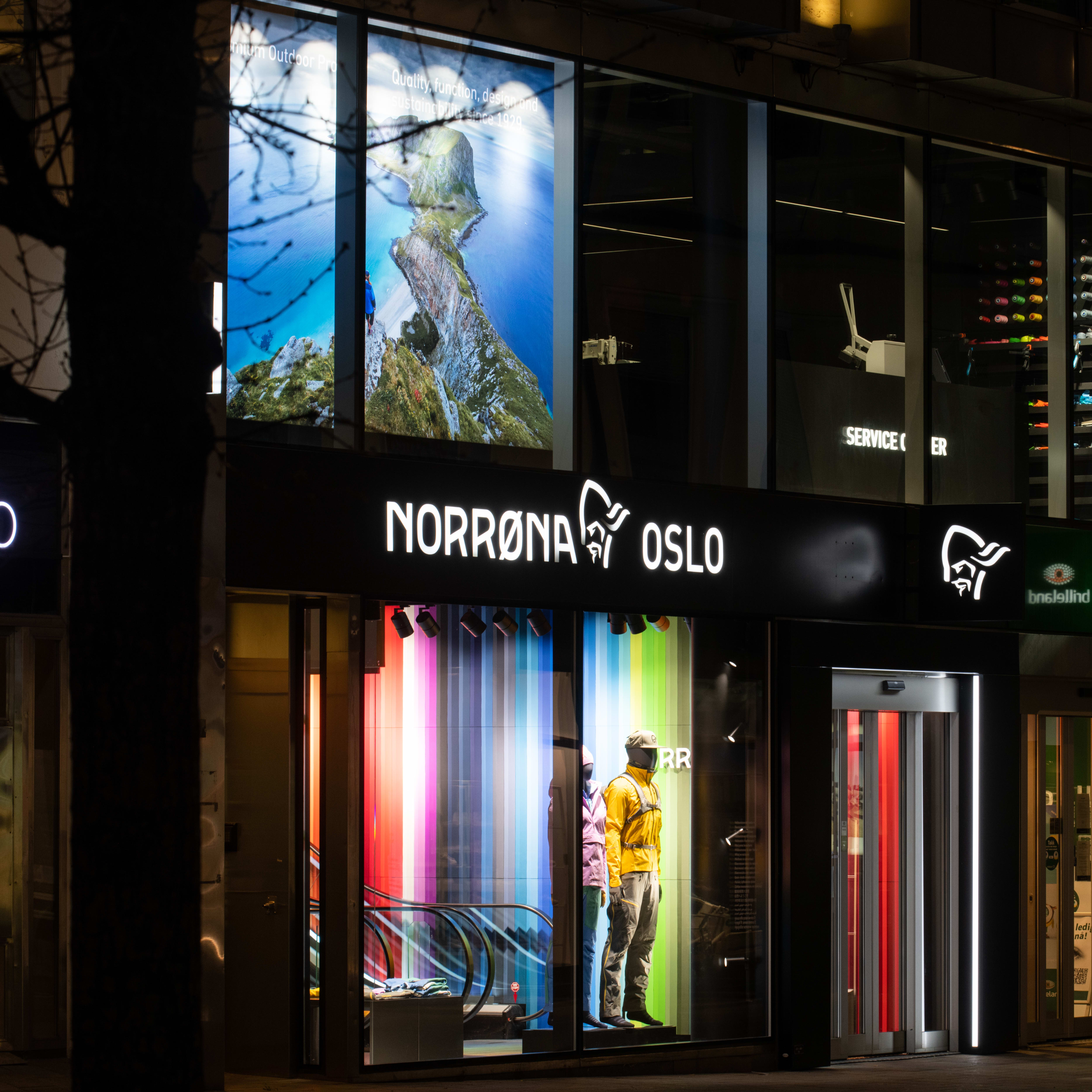 Nighttime view of a Norrøna store in Oslo, Norway, featuring mannequins wearing Norrøna outerwear in the storefront window.
