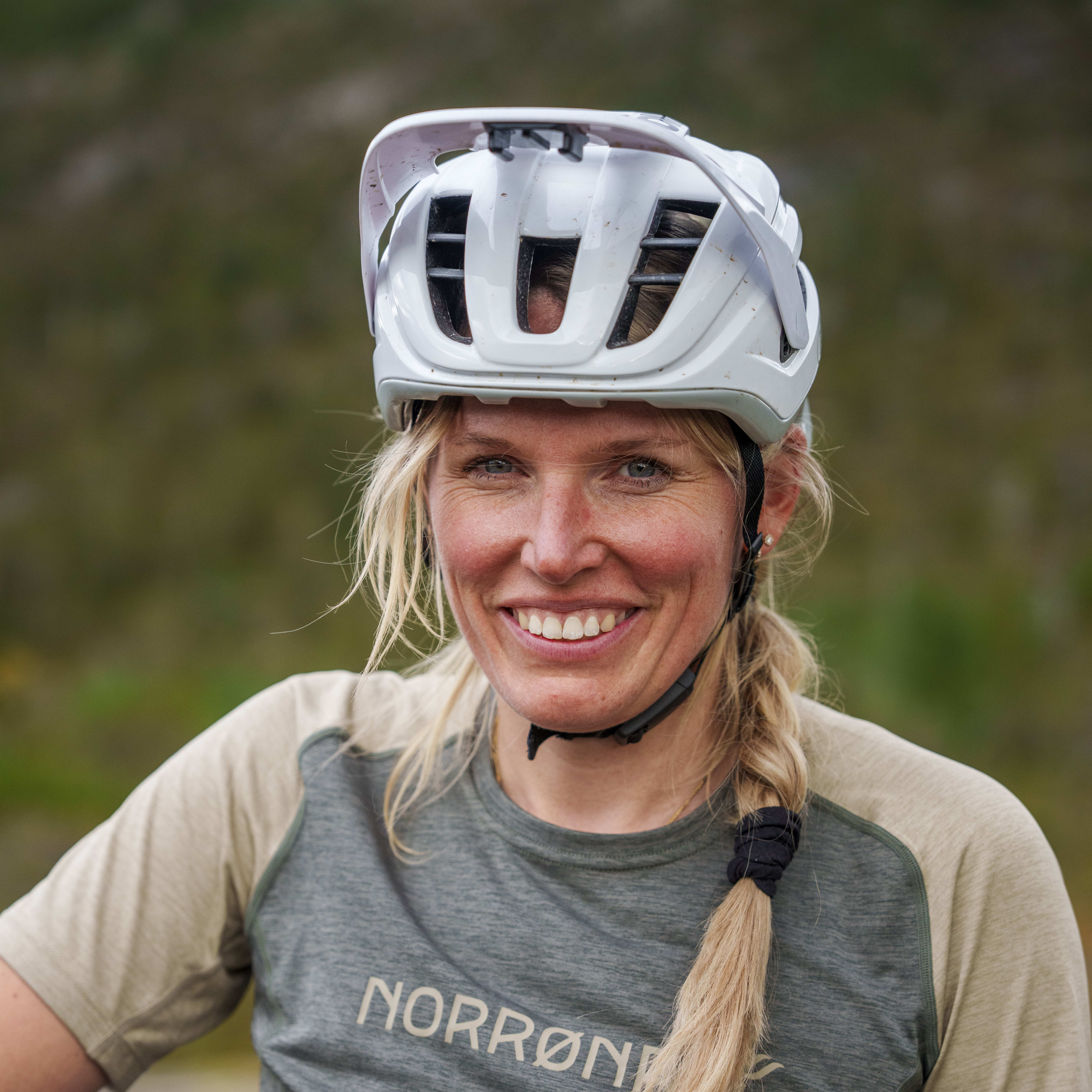 Smiling woman wearing a white helmet and a Norrøna t-shirt.