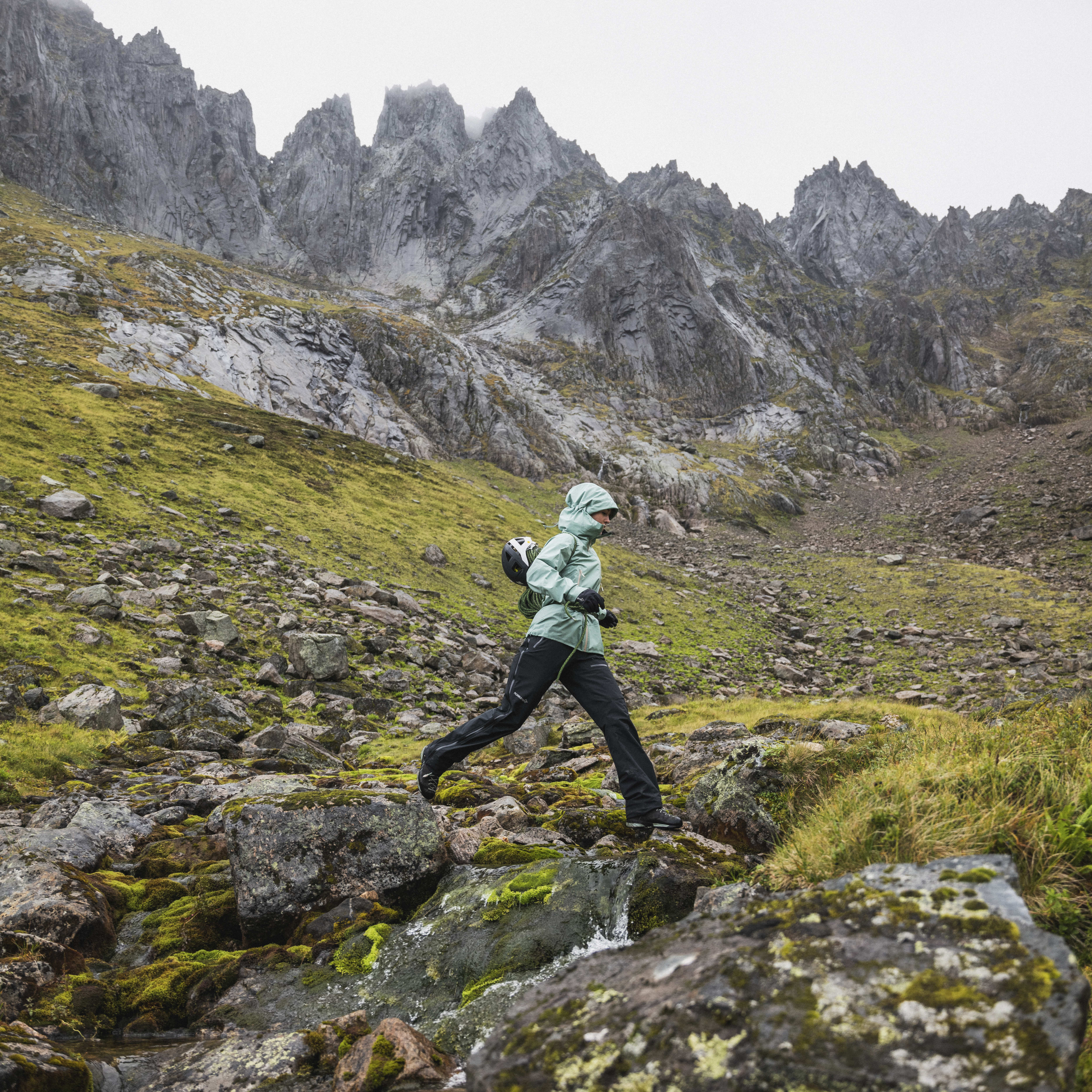 A person in Norrøna clothing runs along a rocky stream in the mountains.
