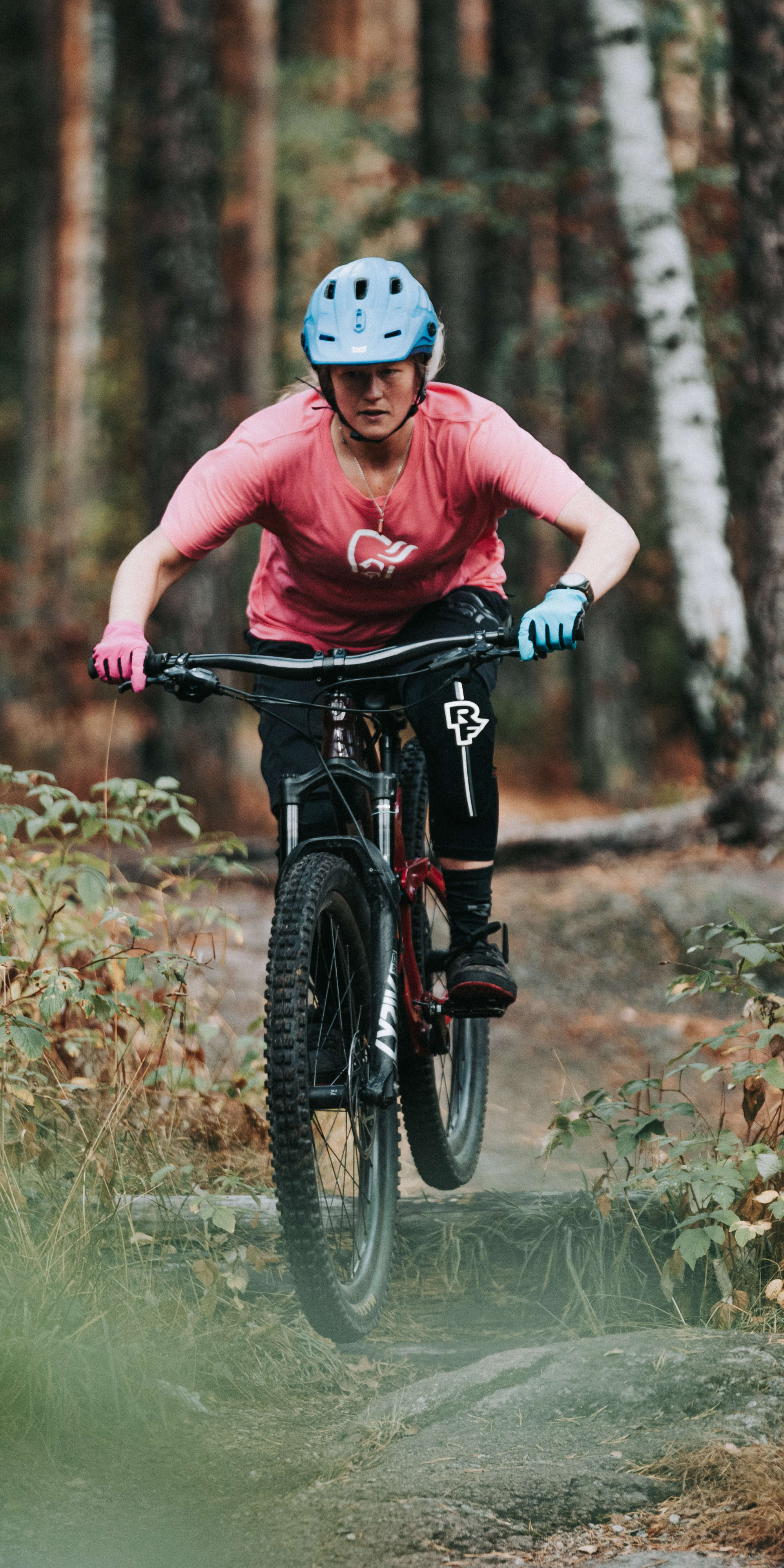 A person wearing a Norrøna shirt and a helmet rides a mountain bike on a trail in the woods. 
