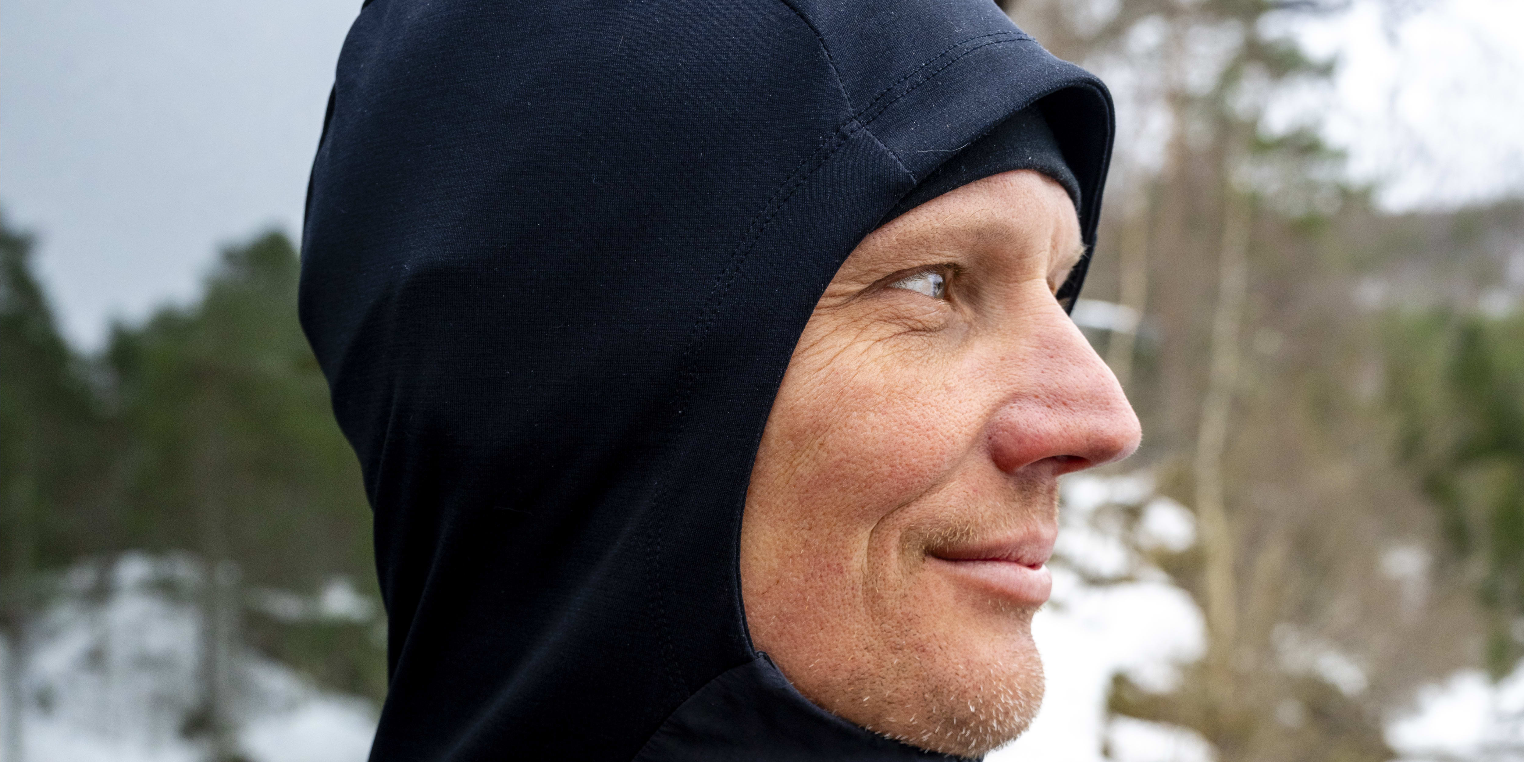 Man wearing a blue Norrøna jacket with the hood up. He is looking to the right of the frame.