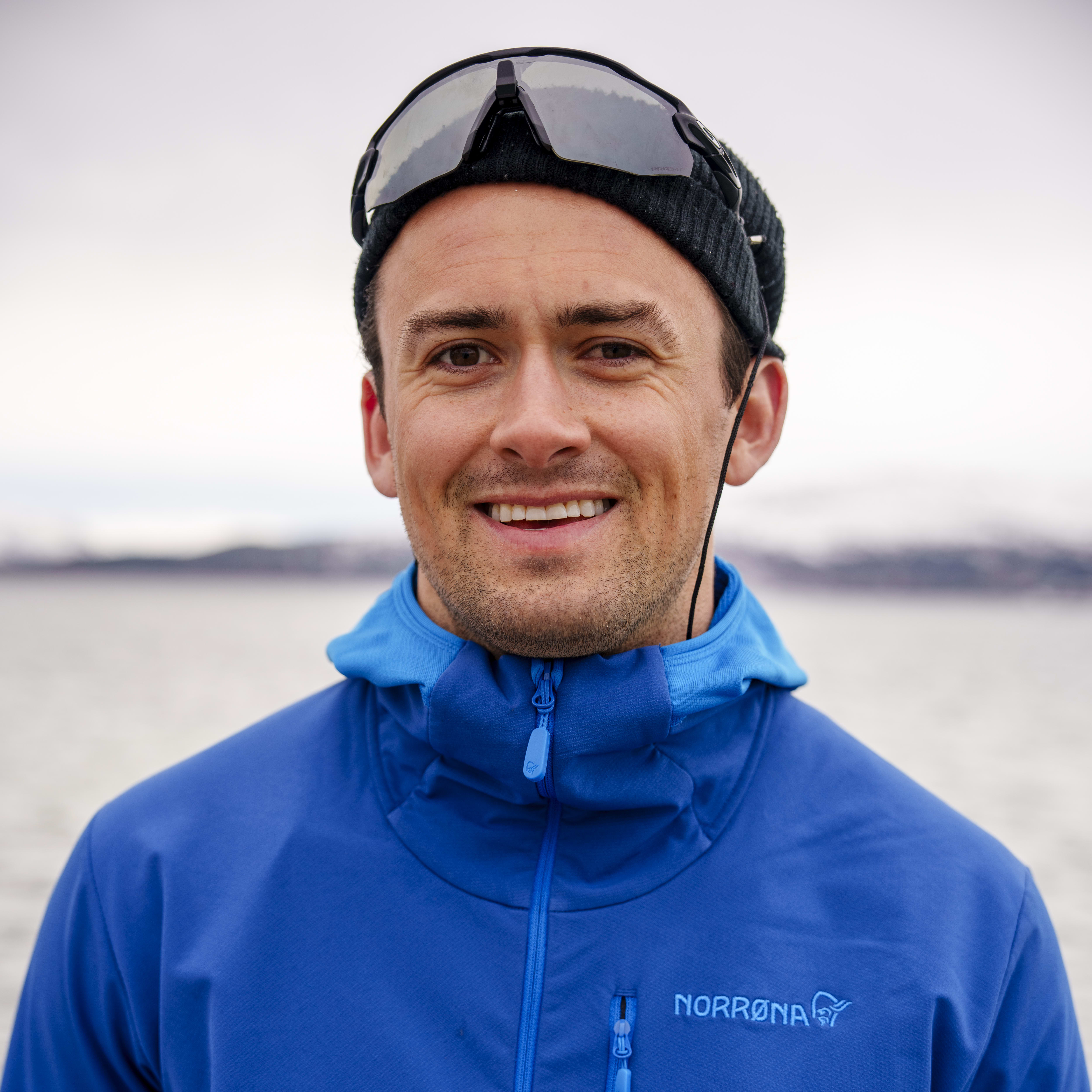 A smiling man wearing a blue Norrøna jacket and sunglasses.