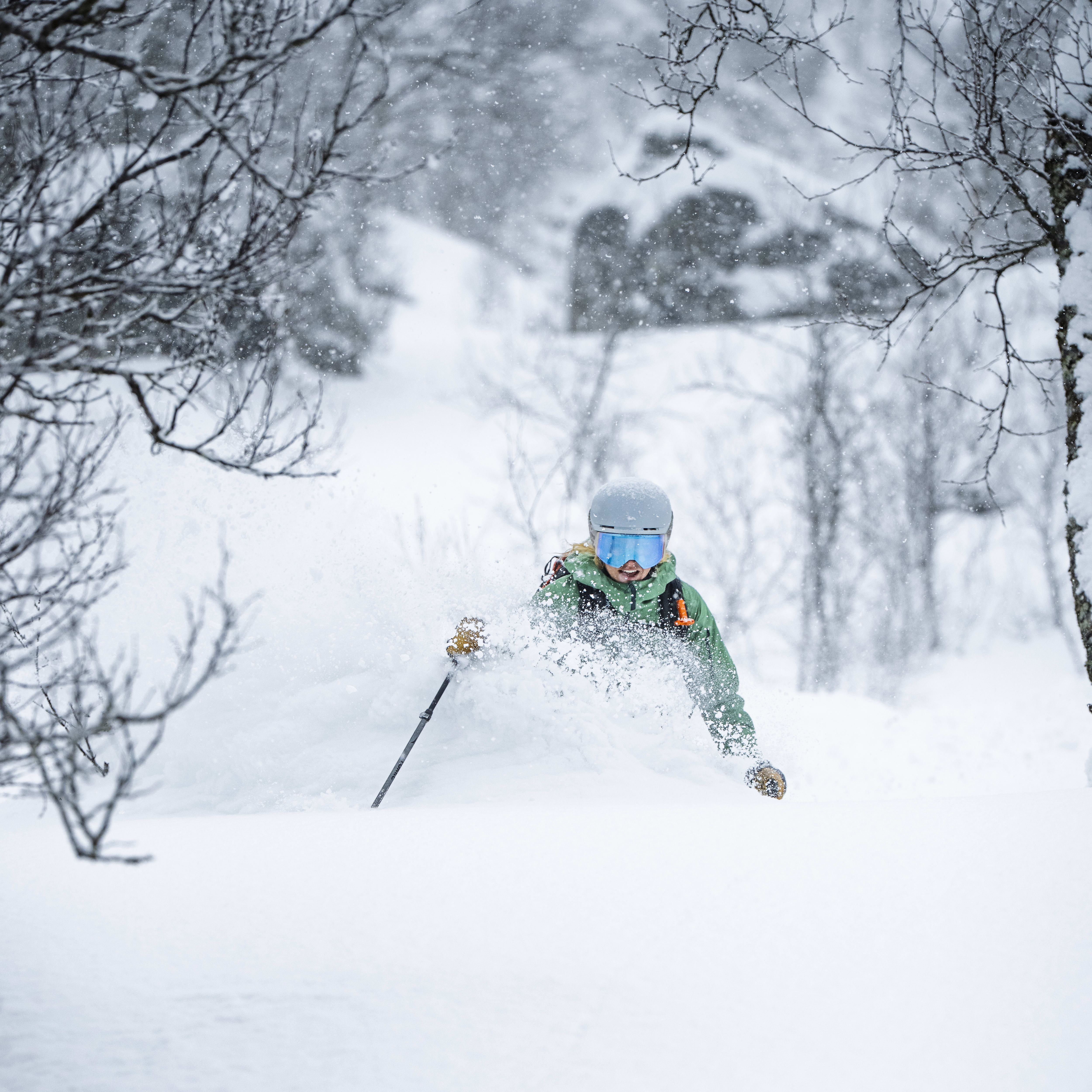 A skier in a Norrøna jacket and helmet skis through deep powder.  
