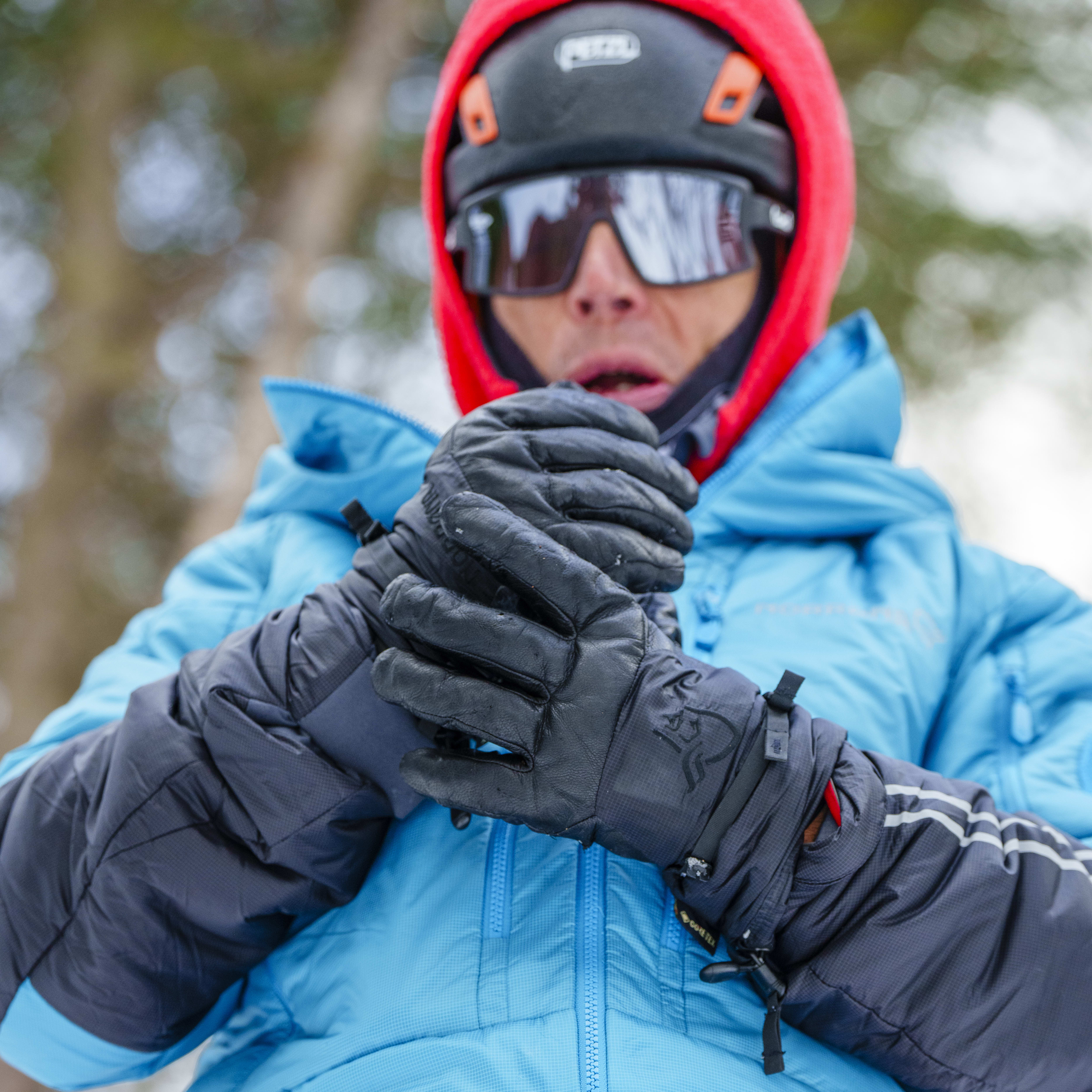 A person wearing a blue Norrøna jacket, red helmet, and black gloves is preparing to climb.  The person has a climbing harness on. 
