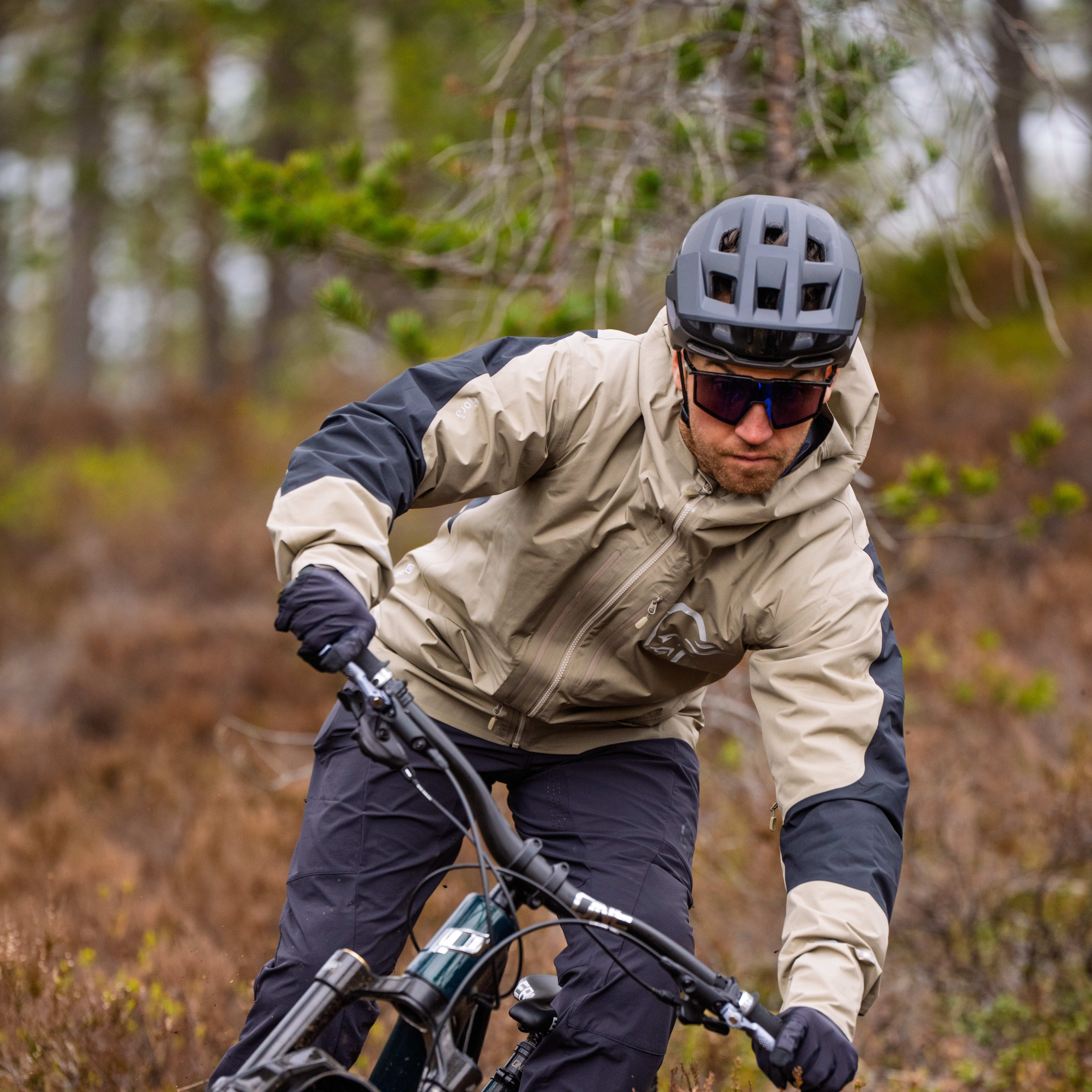 En mountainbiker i en Norrøna-jacka och byxor cyklar på en skogsled.