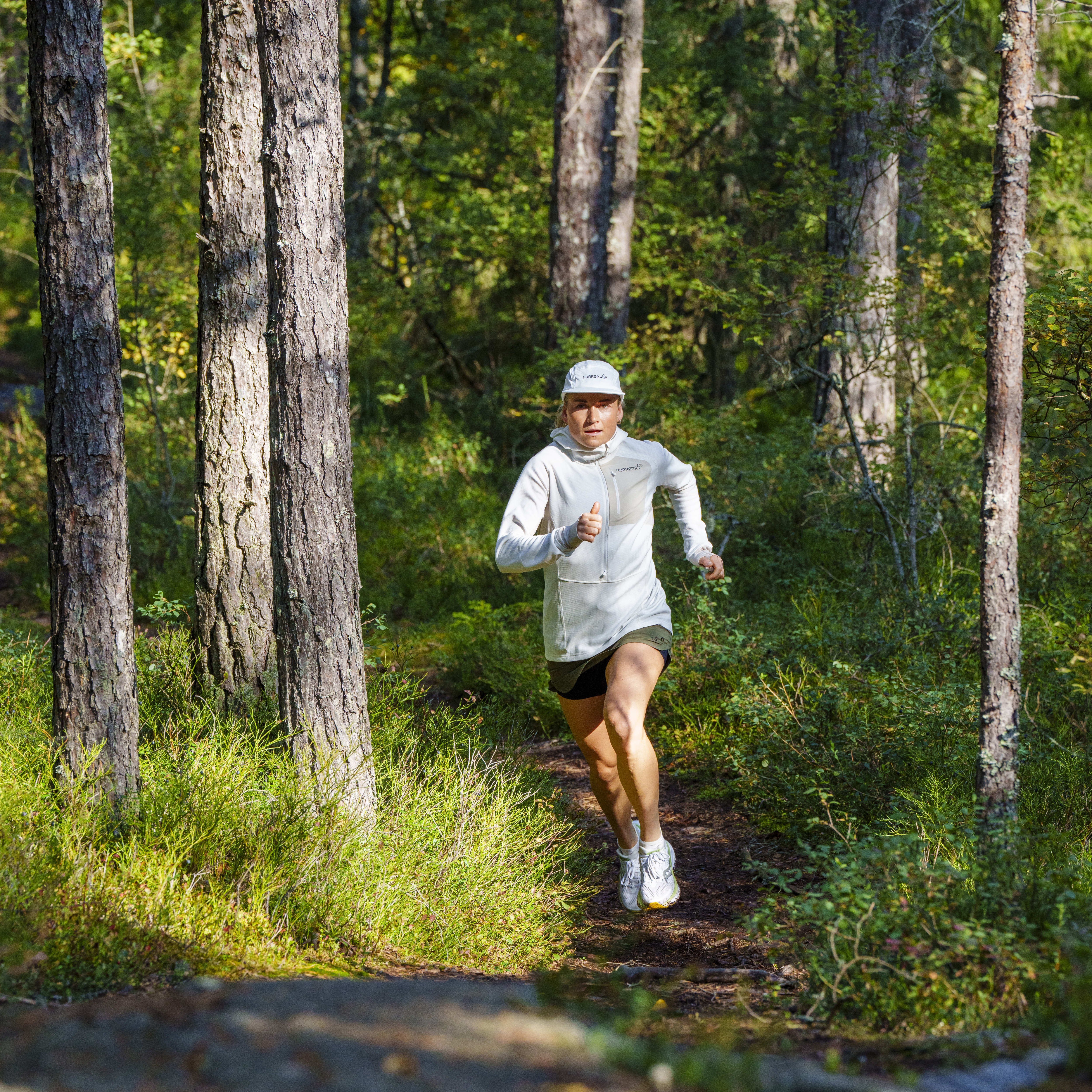 A person wearing a Norrøna hoodie runs on a forest path.