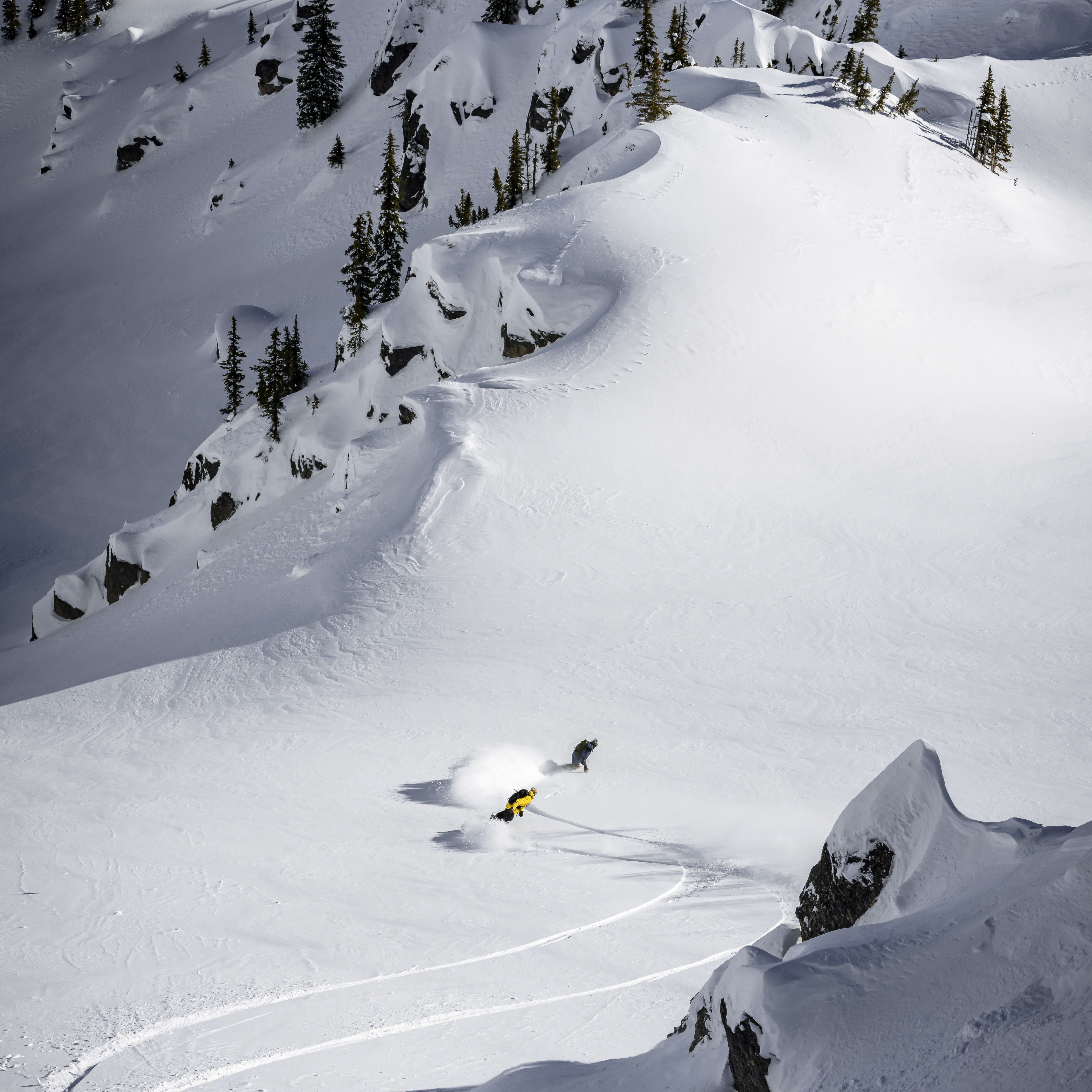 Two snowboarders carving through fresh powder in a snowy mountain scene.