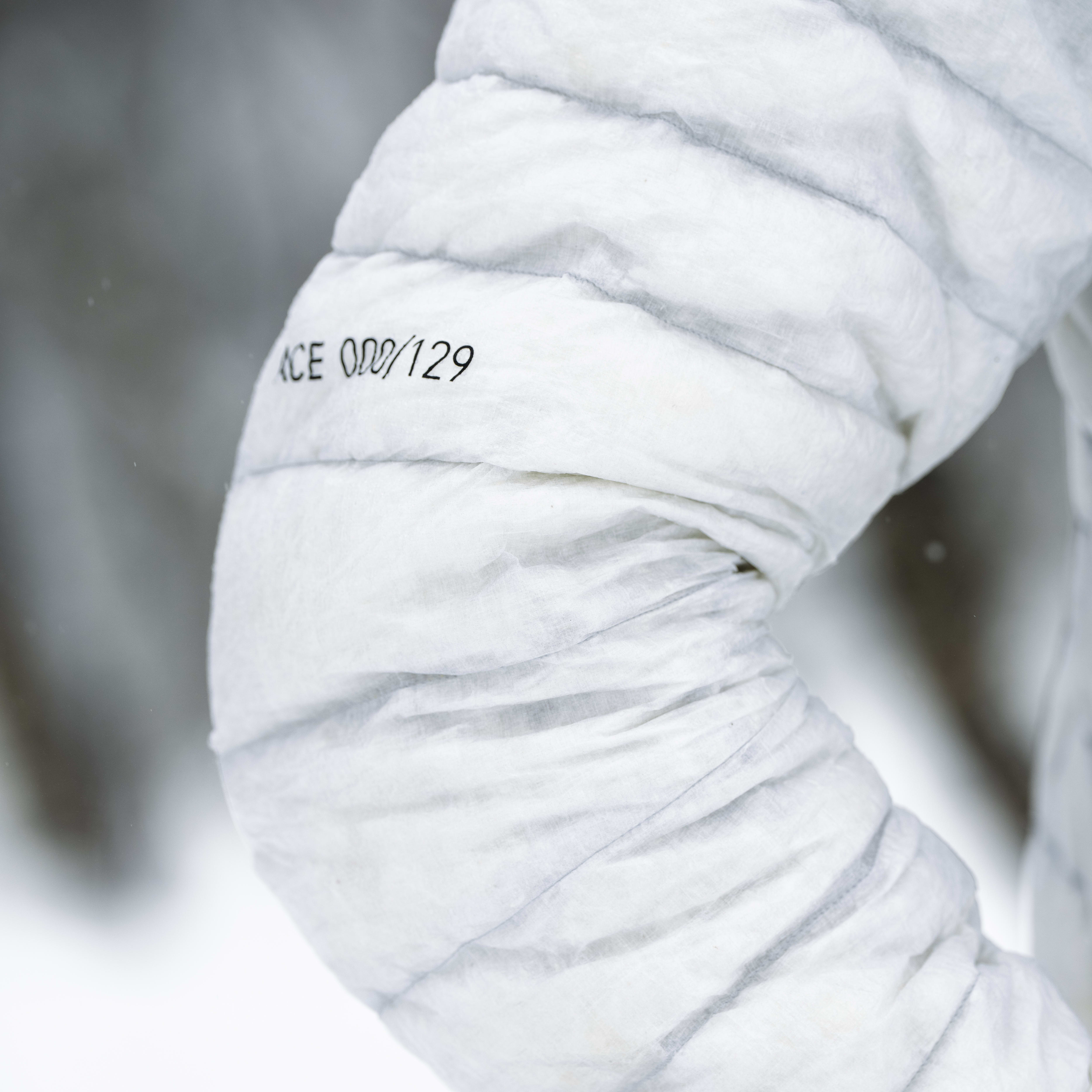 Close up of a white Norrøna jacket sleeve. The sleeve is quilted and has a black tag with the number 00/129 on it.