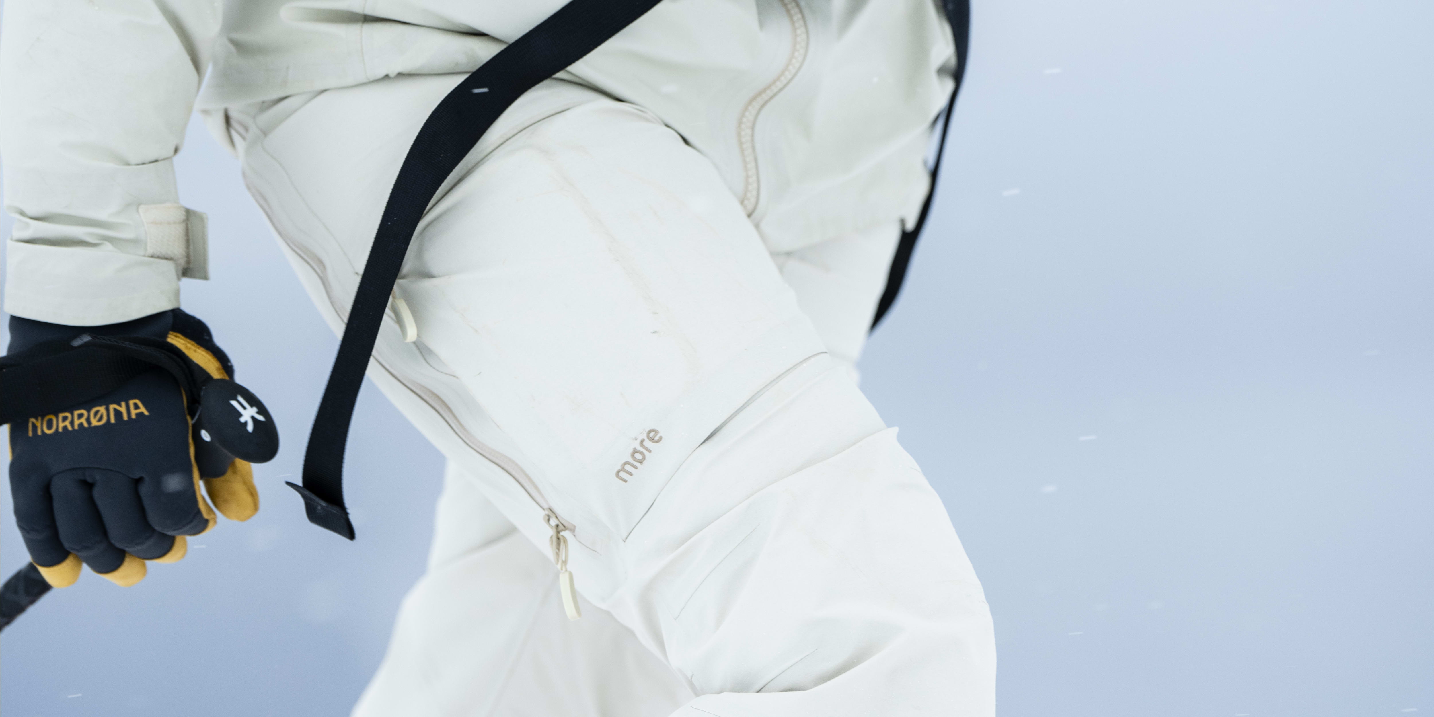 Person wearing a white Norrøna ski suit and gloves, standing in snow.