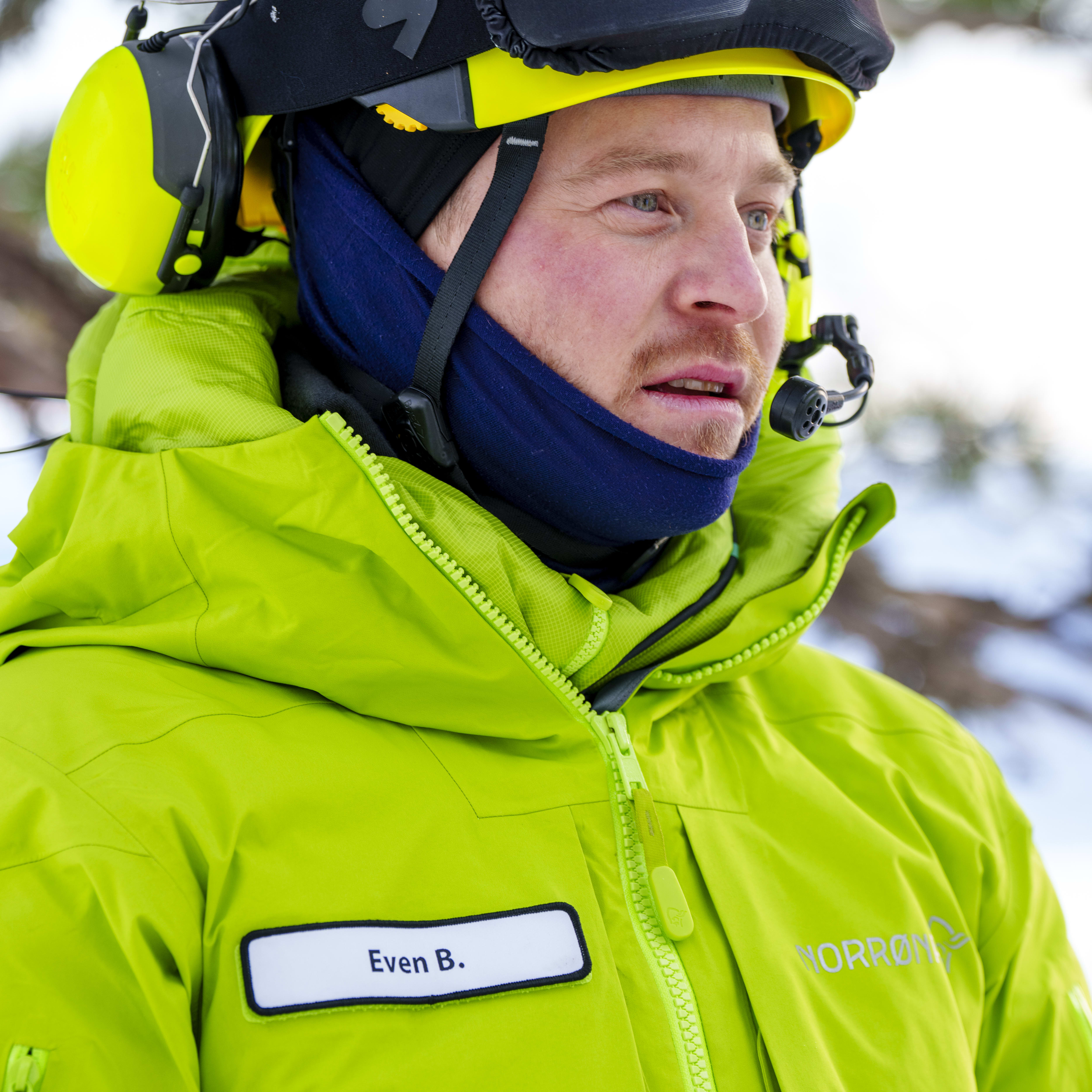 A man wearing a bright green Norrøna jacket and a yellow helmet. He is looking off to the side.