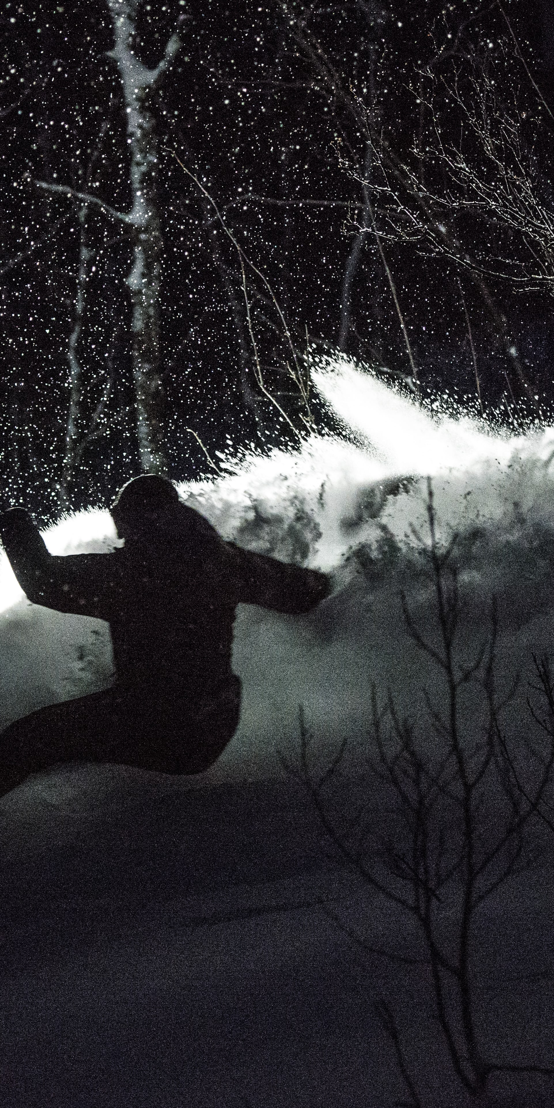 Silhouette of a snowboarder wearing Norrøna clothing, riding a snowboard downhill in the snow. 
