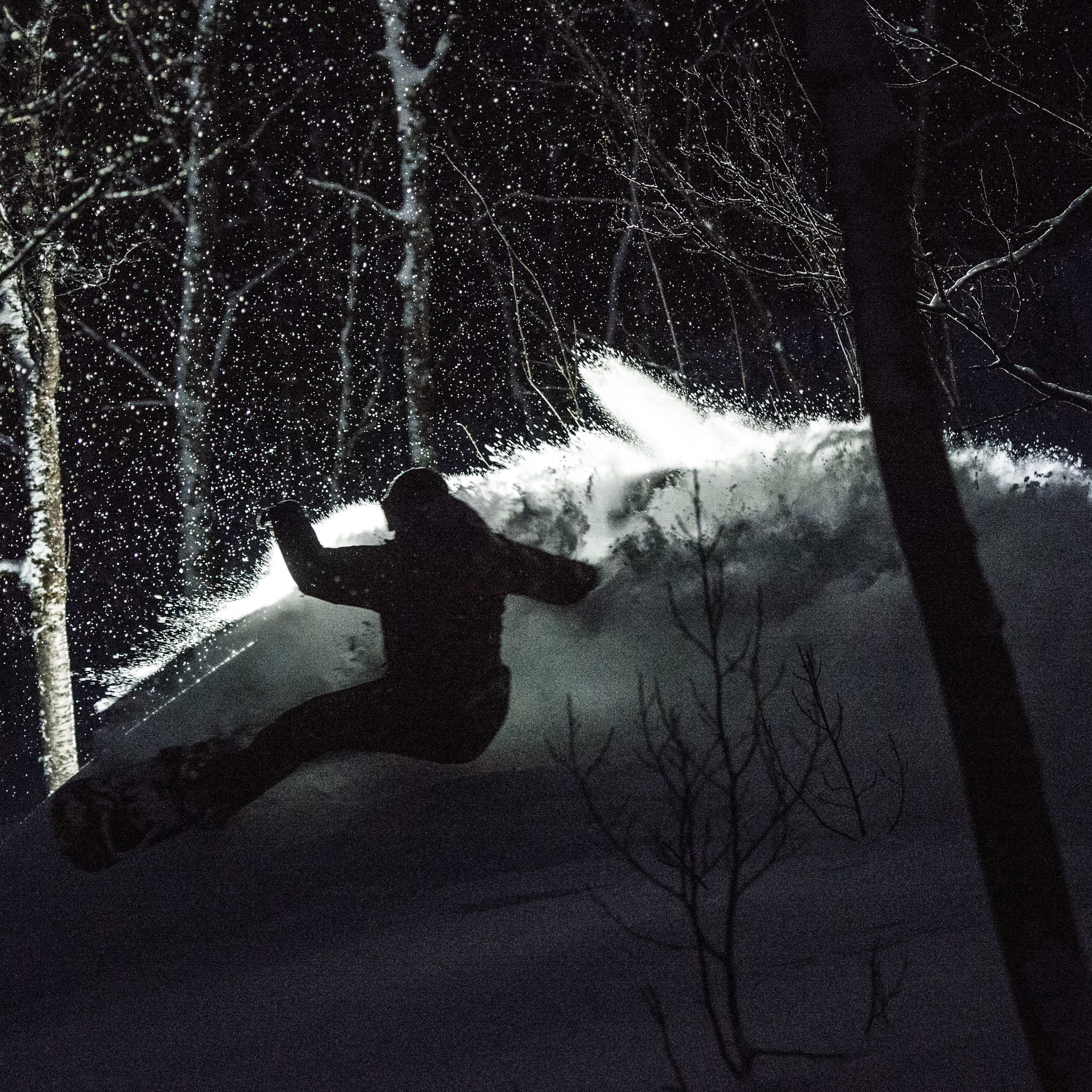 Silhouette of a snowboarder wearing Norrøna clothing, riding a snowboard downhill in the snow.