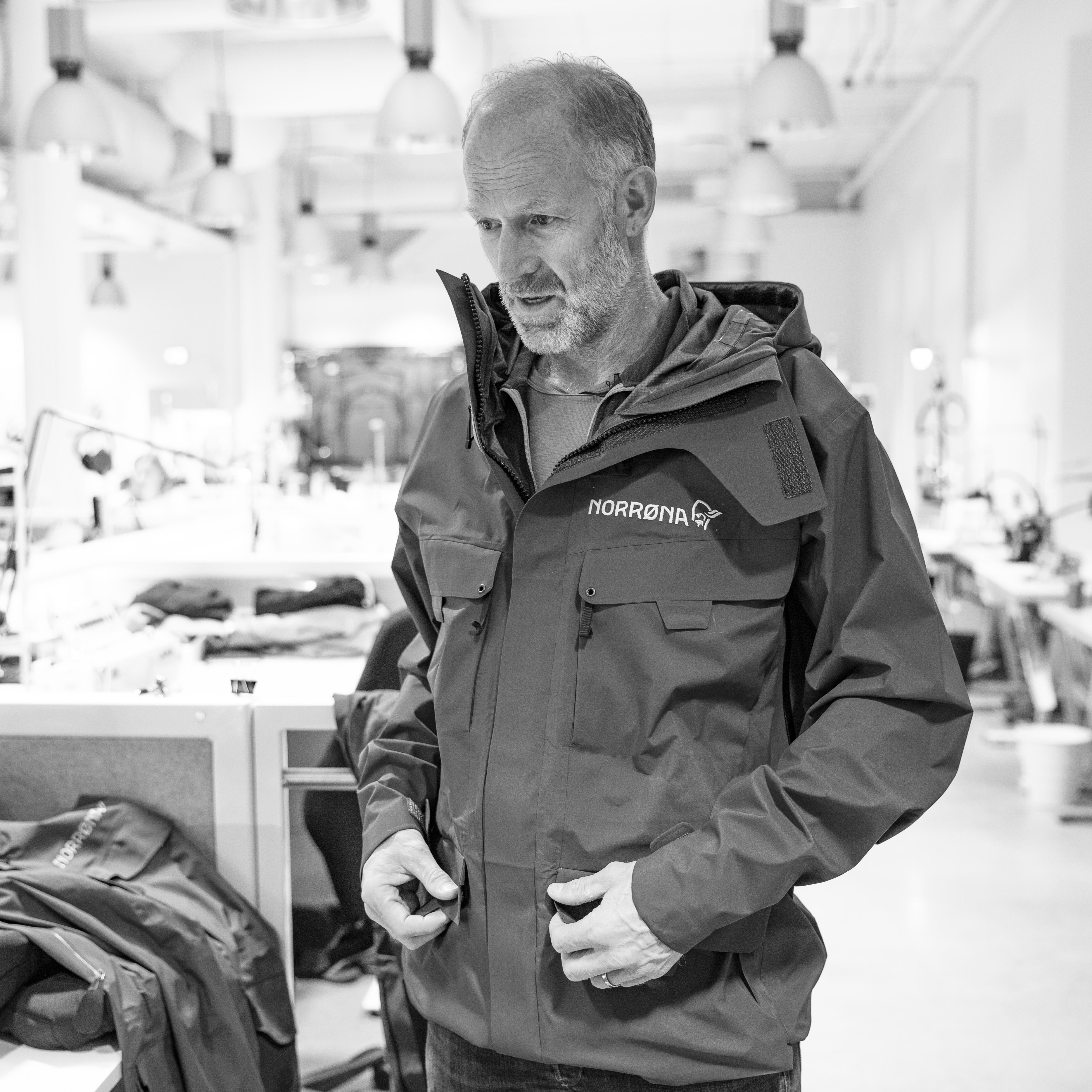 A man wearing a Norrøna jacket with his hands in the pockets.  The background is blurred. 
