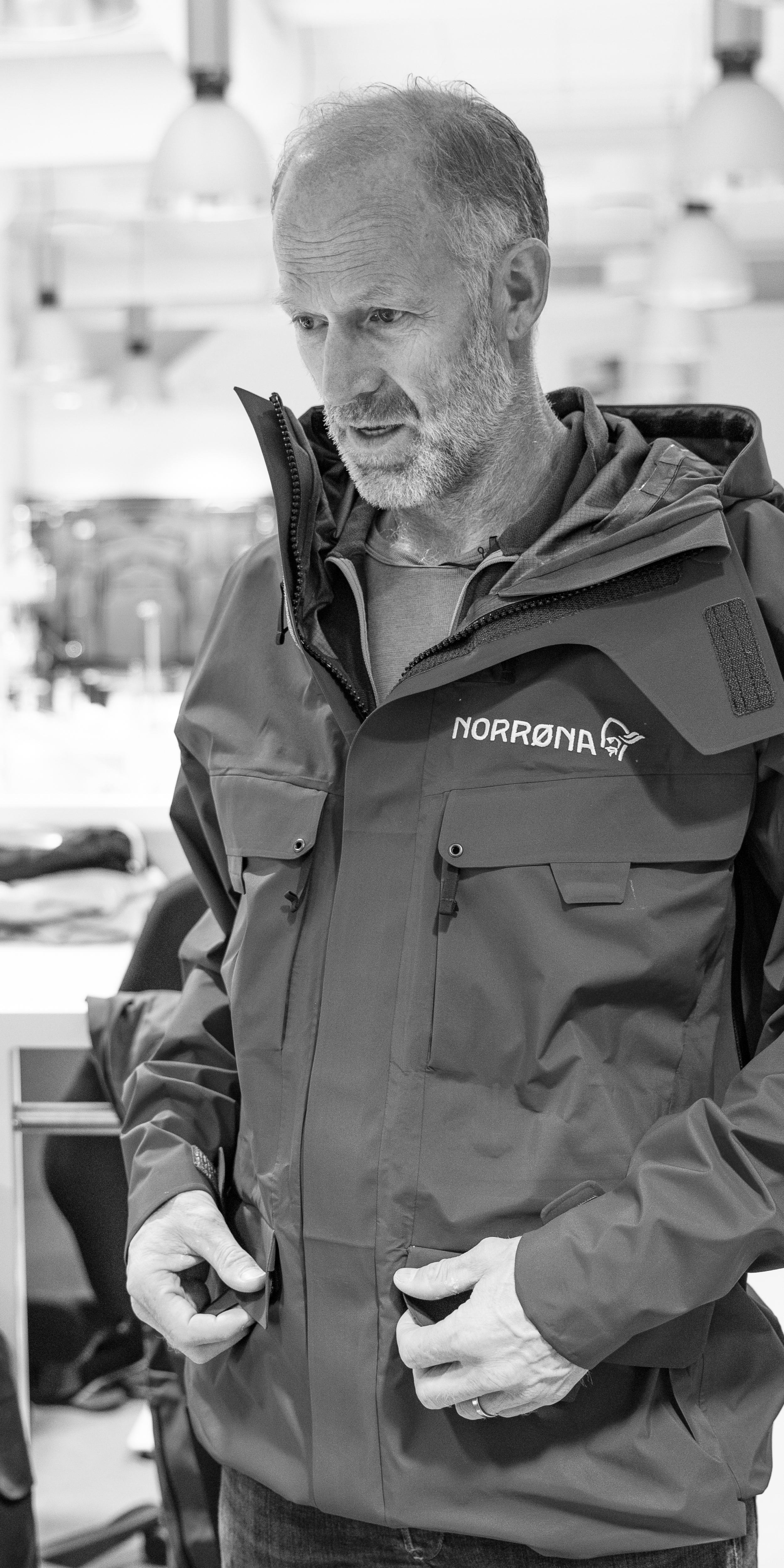 A man wearing a Norrøna jacket with his hands in the pockets.  The background is blurred. 
