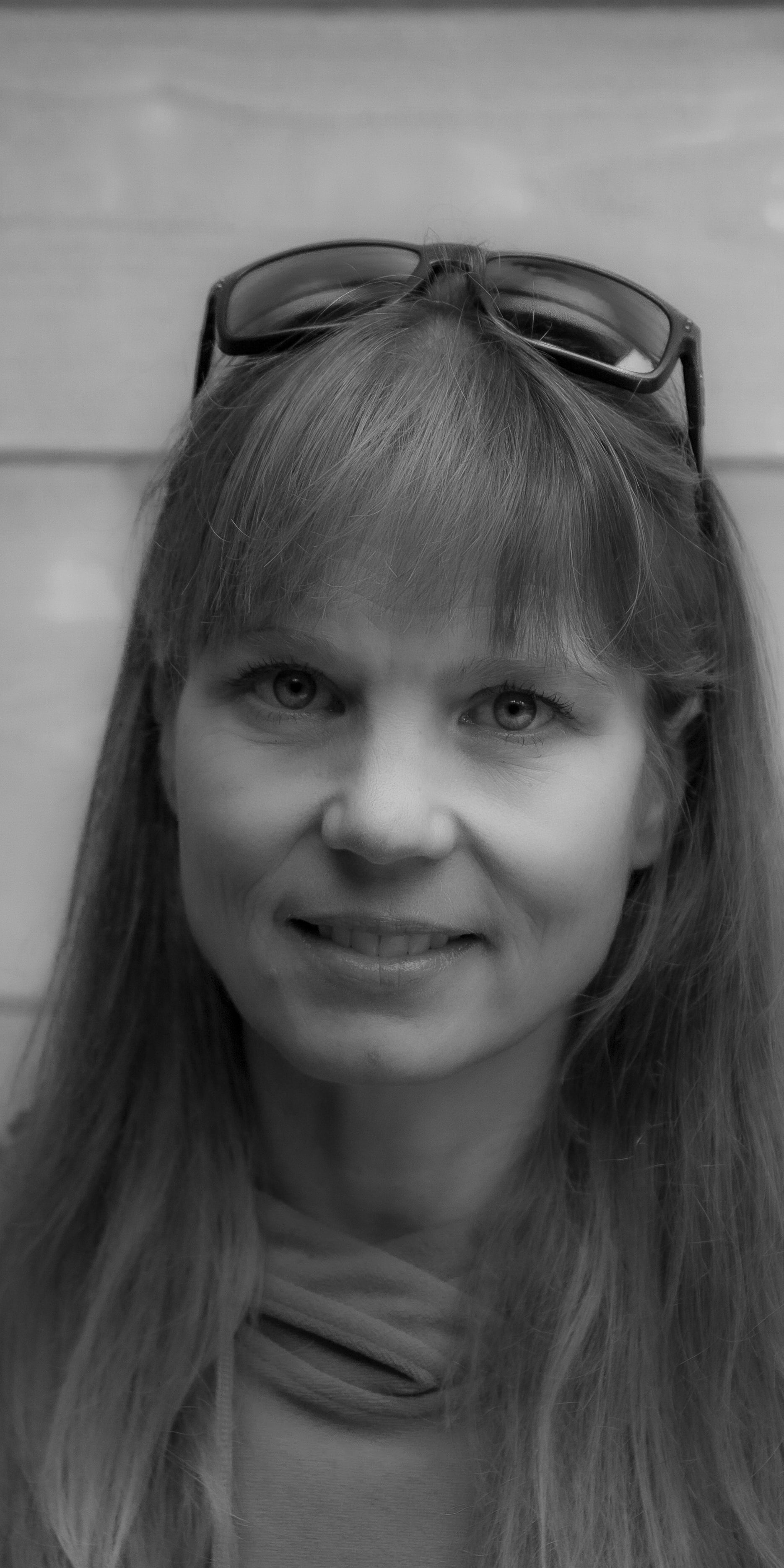 A woman with long hair wearing a Norrøna hoodie and sunglasses smiles at the camera. 

