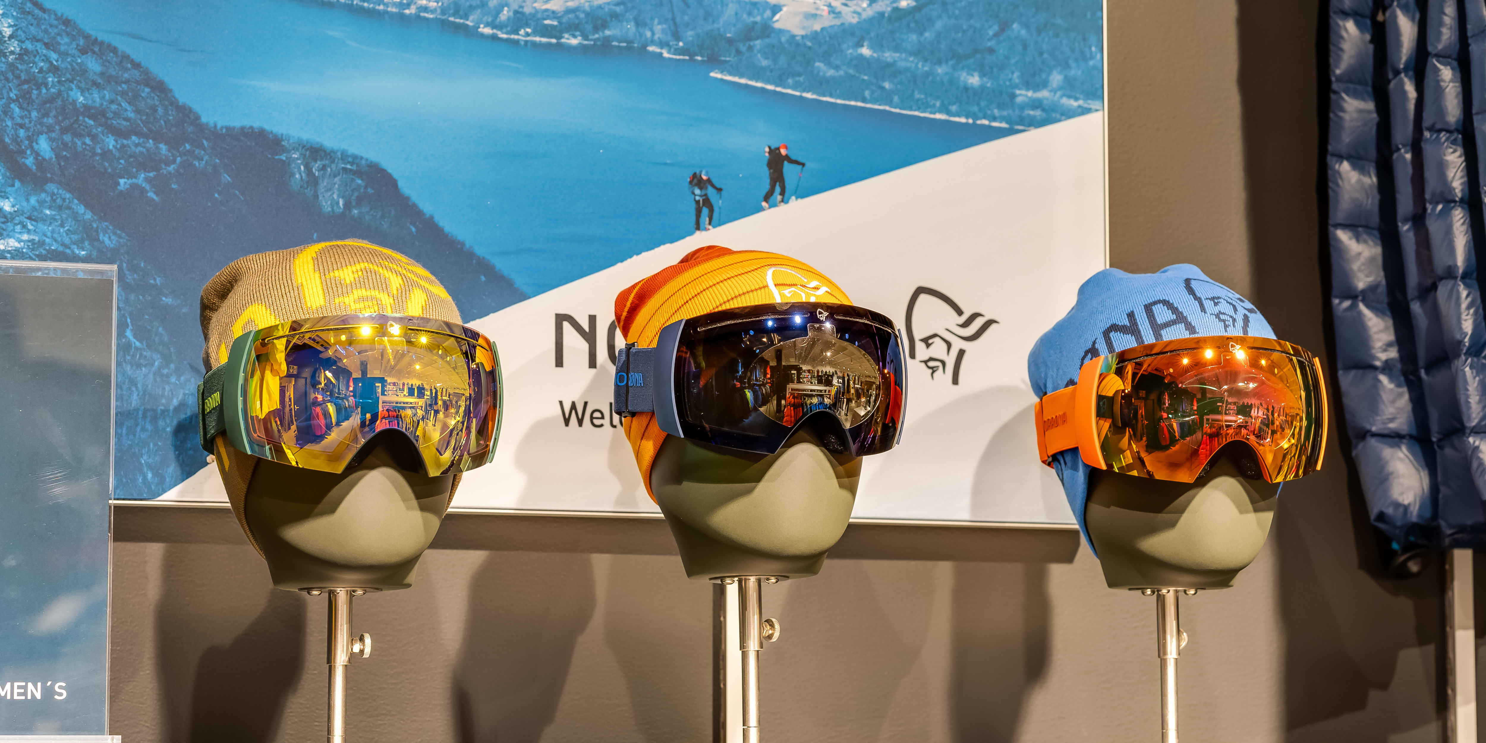 Norrøna ski goggles and beanies displayed on three mannequin heads.