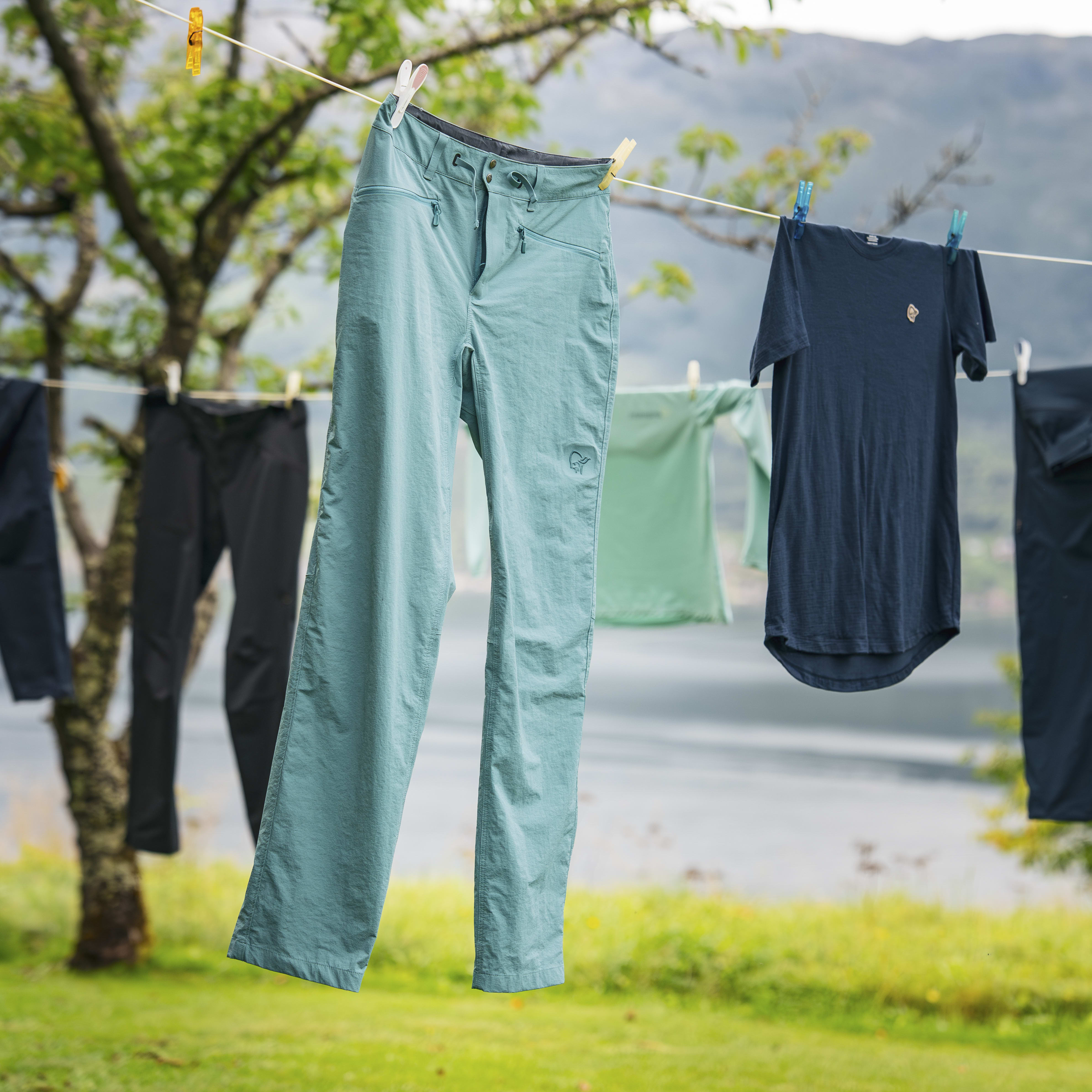 Outdoor laundry line with various Norrøna clothing items, including teal pants and a navy tee, drying against a scenic landscape.