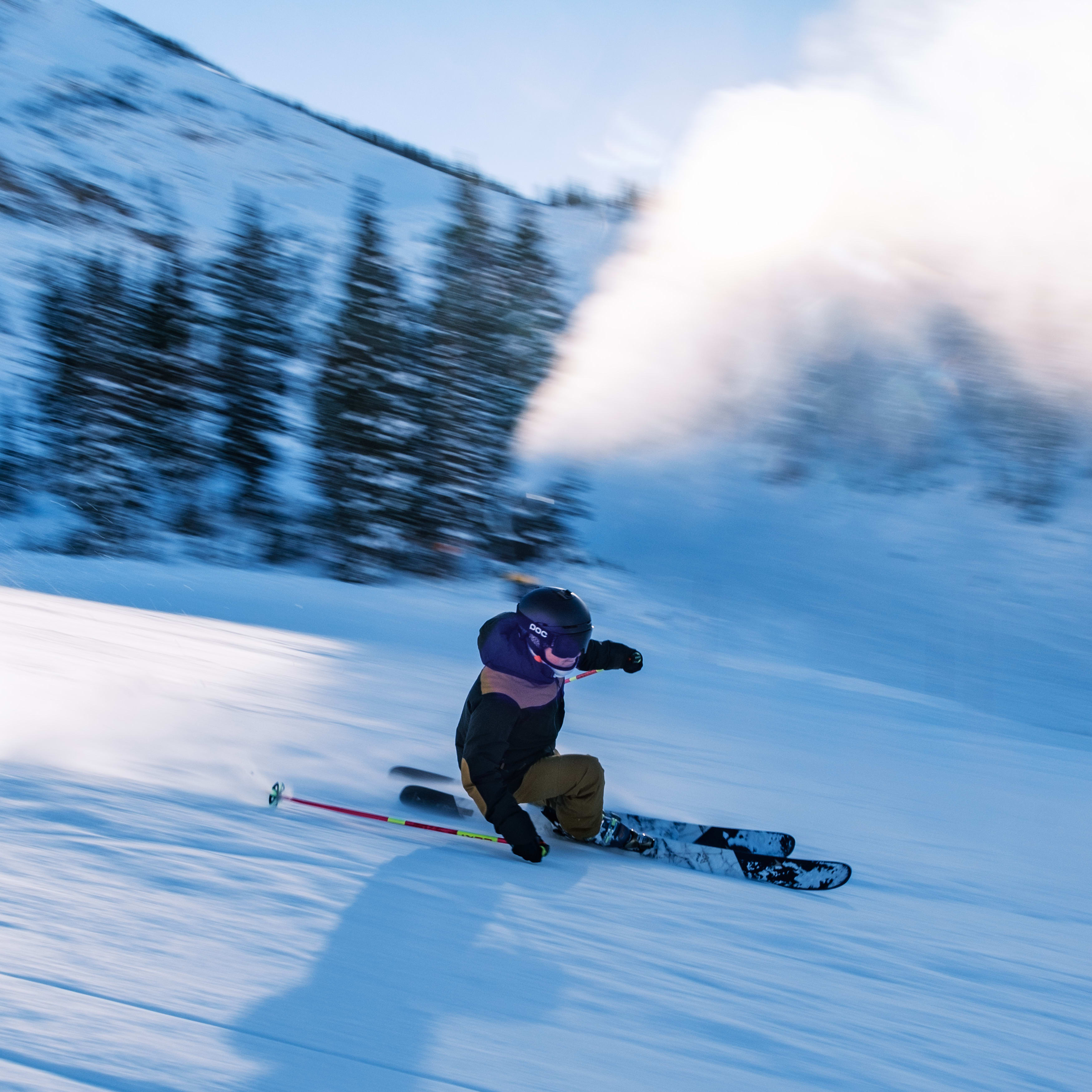 A skier wearing a Norrøna jacket speeds down a snowy slope. The skier is wearing a helmet.  
