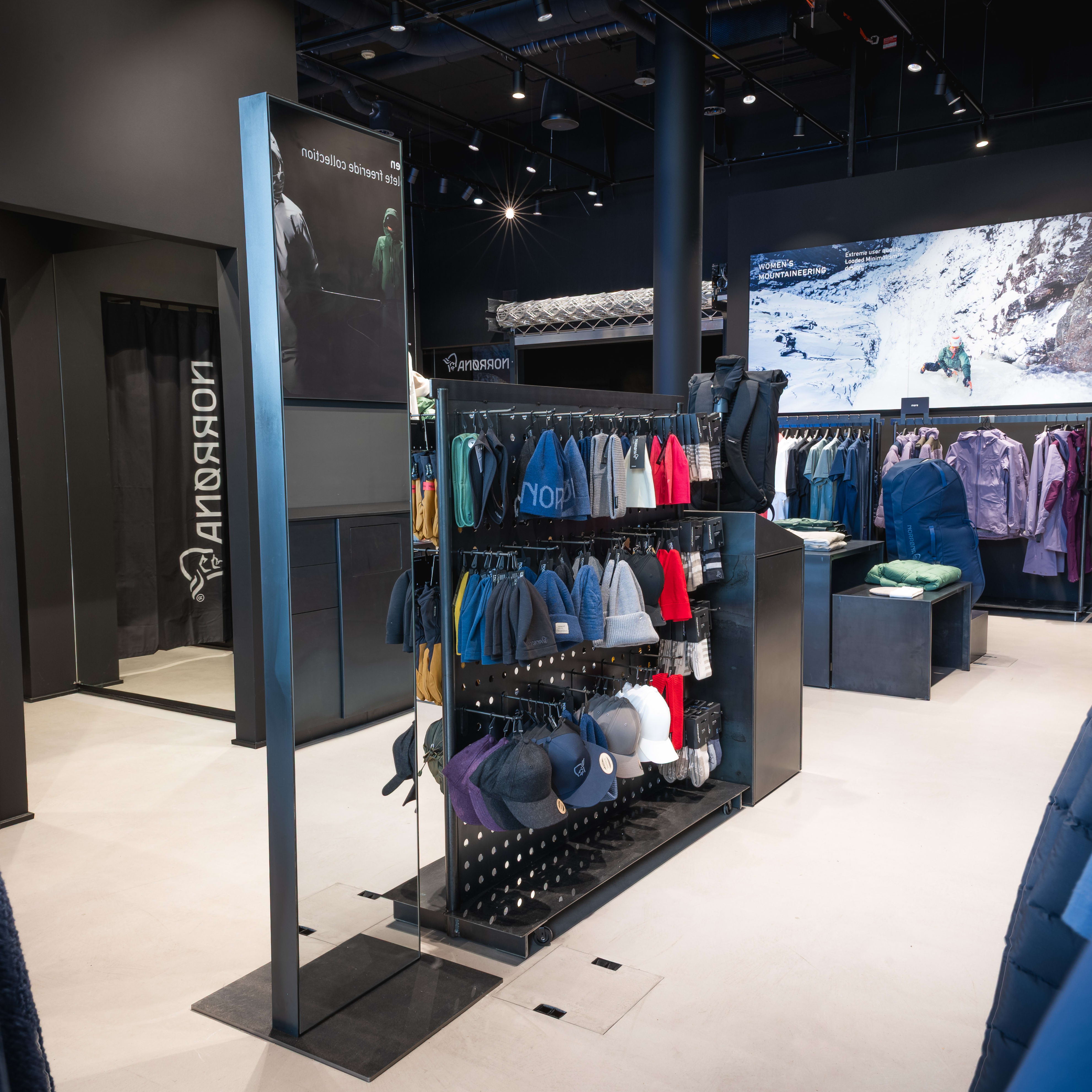 Interior view of a Norrøna clothing store. Racks display apparel, including hats and jackets. A screen shows mountain scenery.