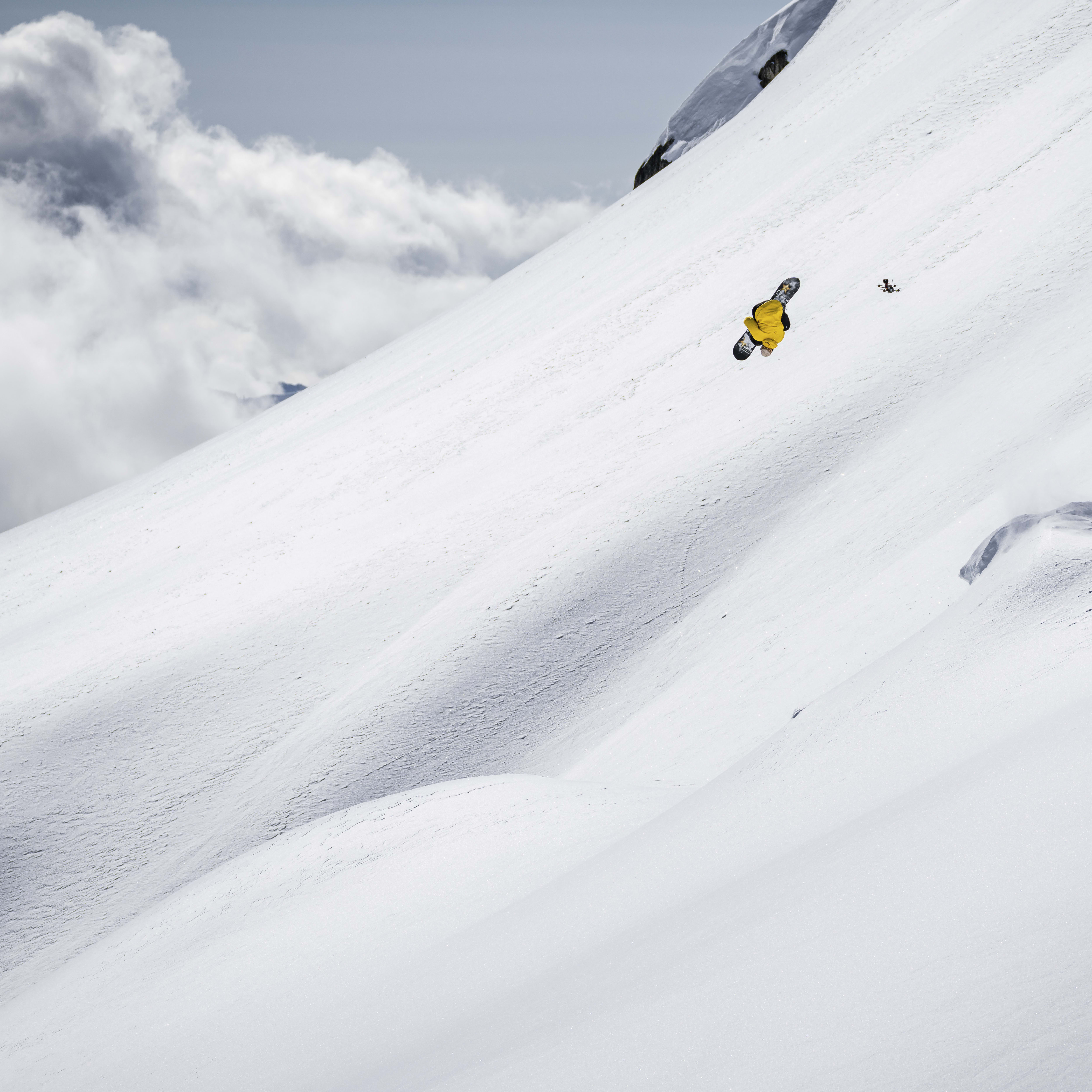A person in a yellow jacket snowboards down a snowy mountainside.