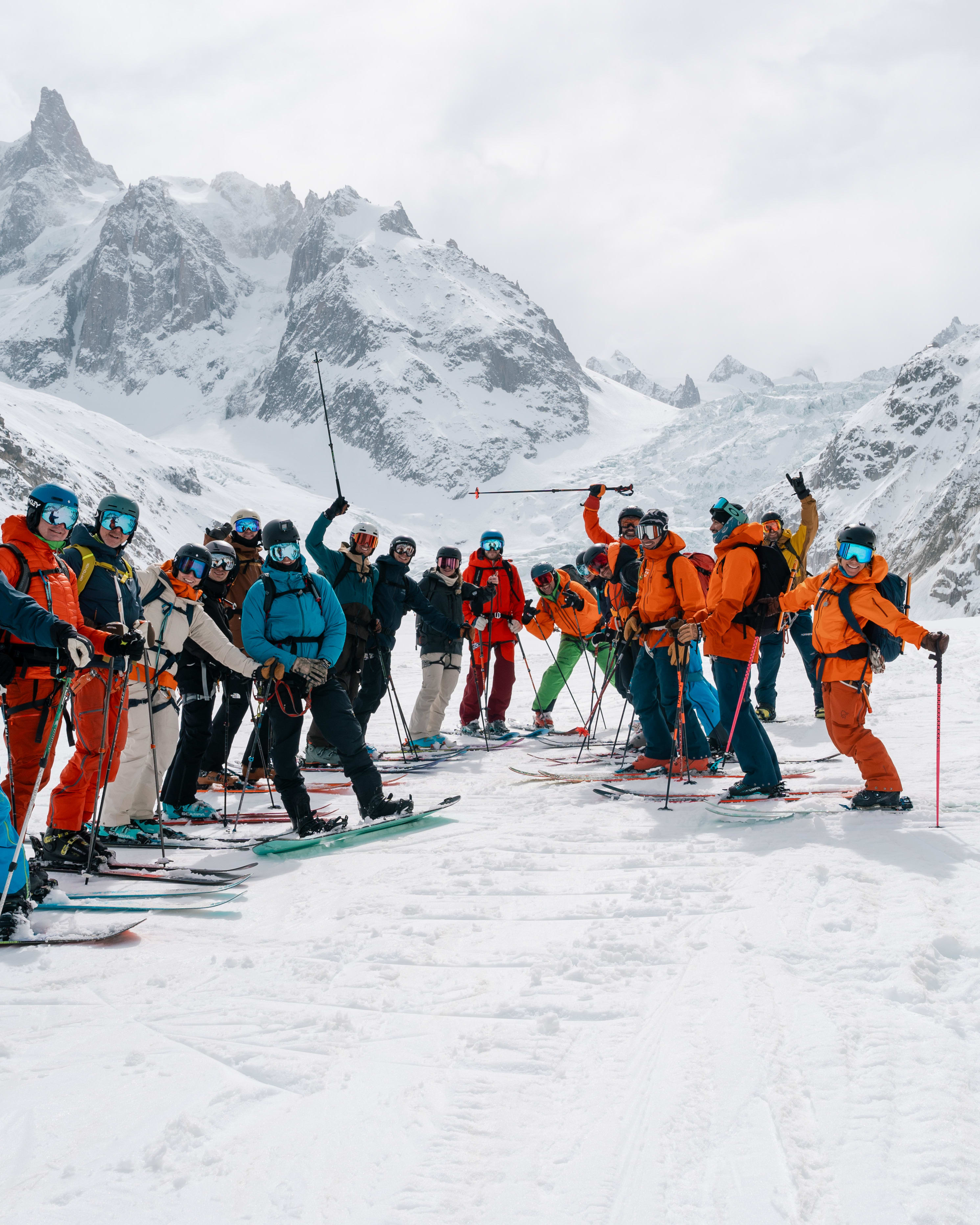 A group of skiers wearing Norrøna outerwear pose on snow with mountain peaks in the background on a cloudy day.