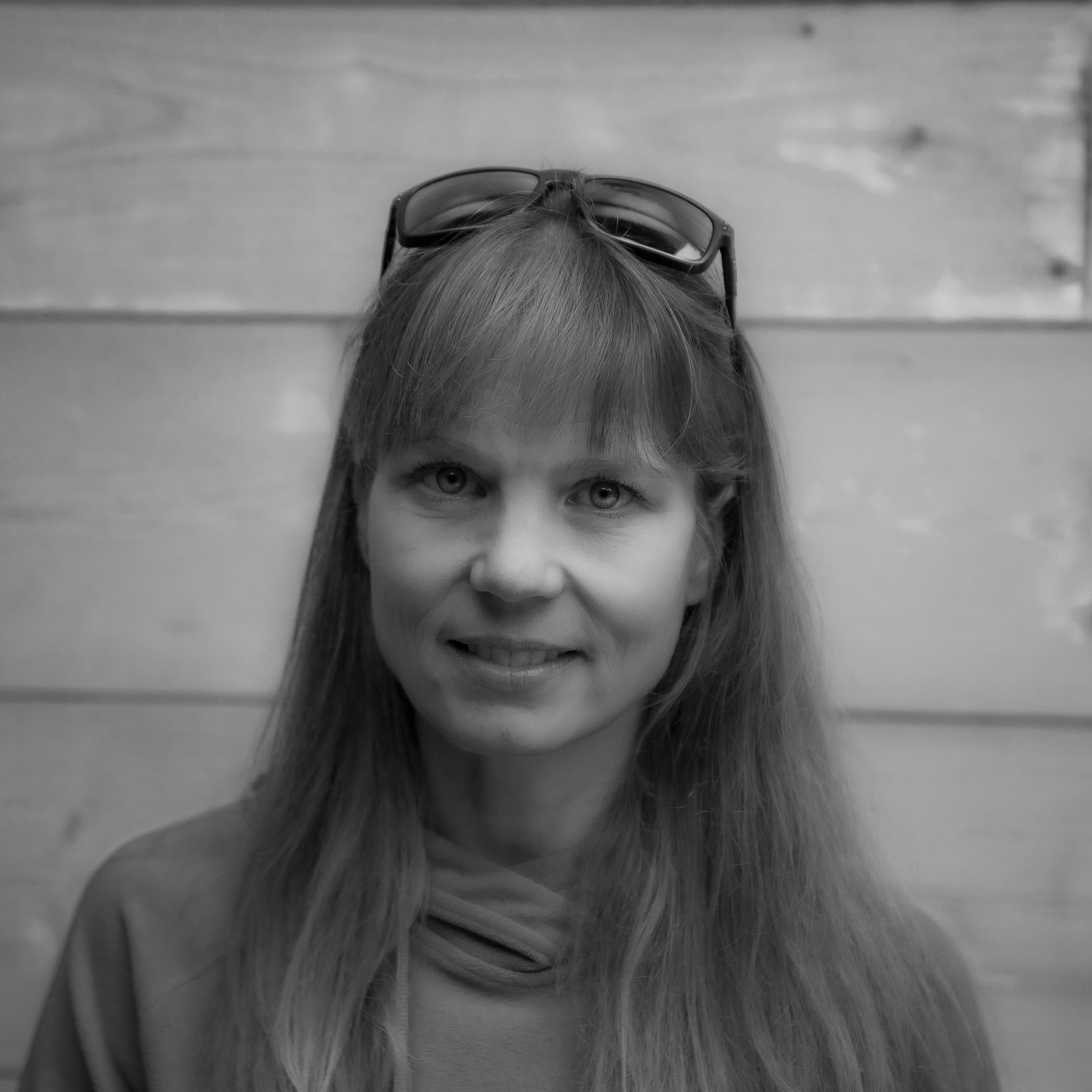 A woman with long hair wearing a Norrøna hoodie and sunglasses smiles at the camera.