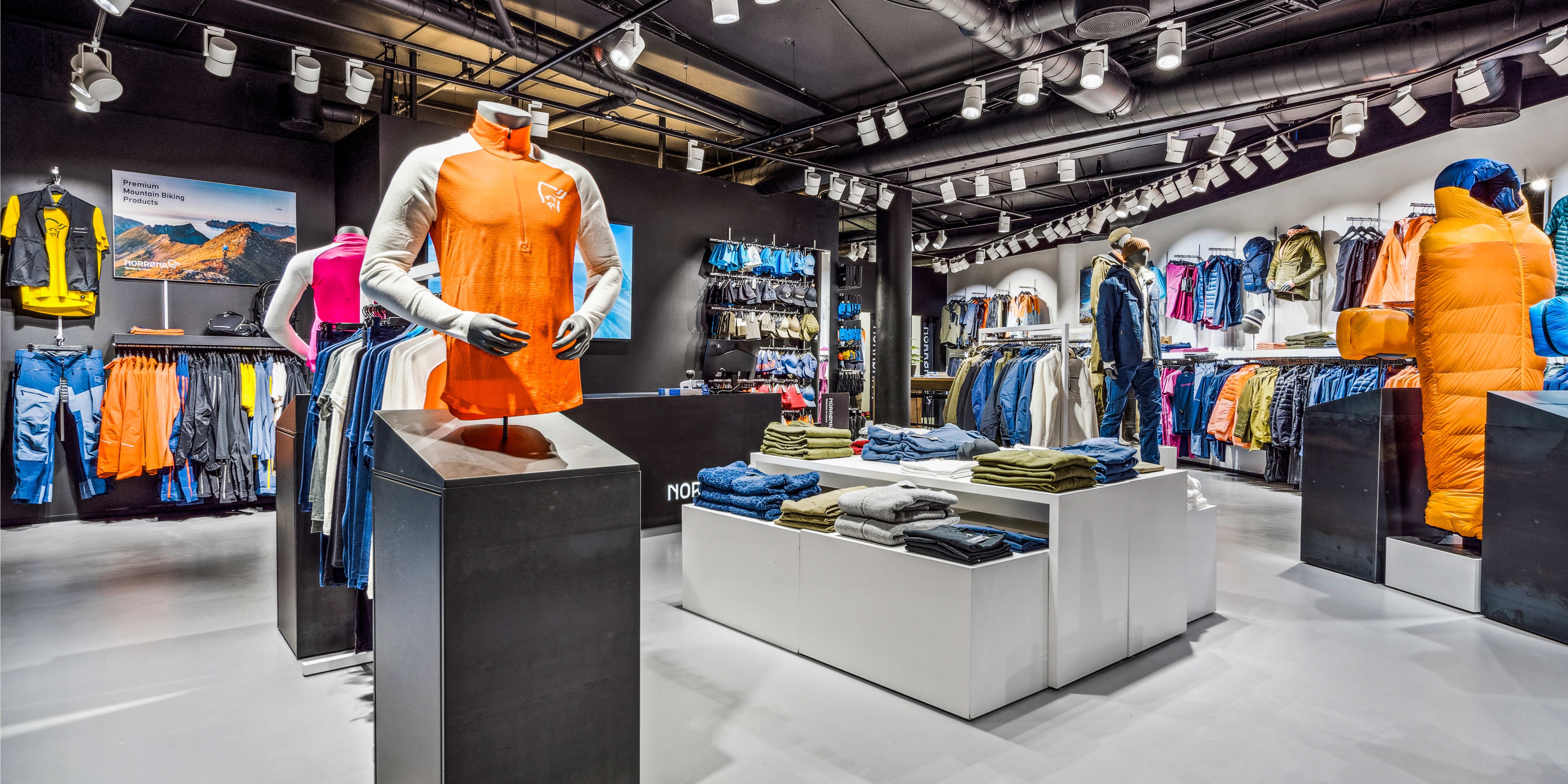 A modern Norrøna retail store displaying outdoor clothing on mannequins, display tables, and racks.