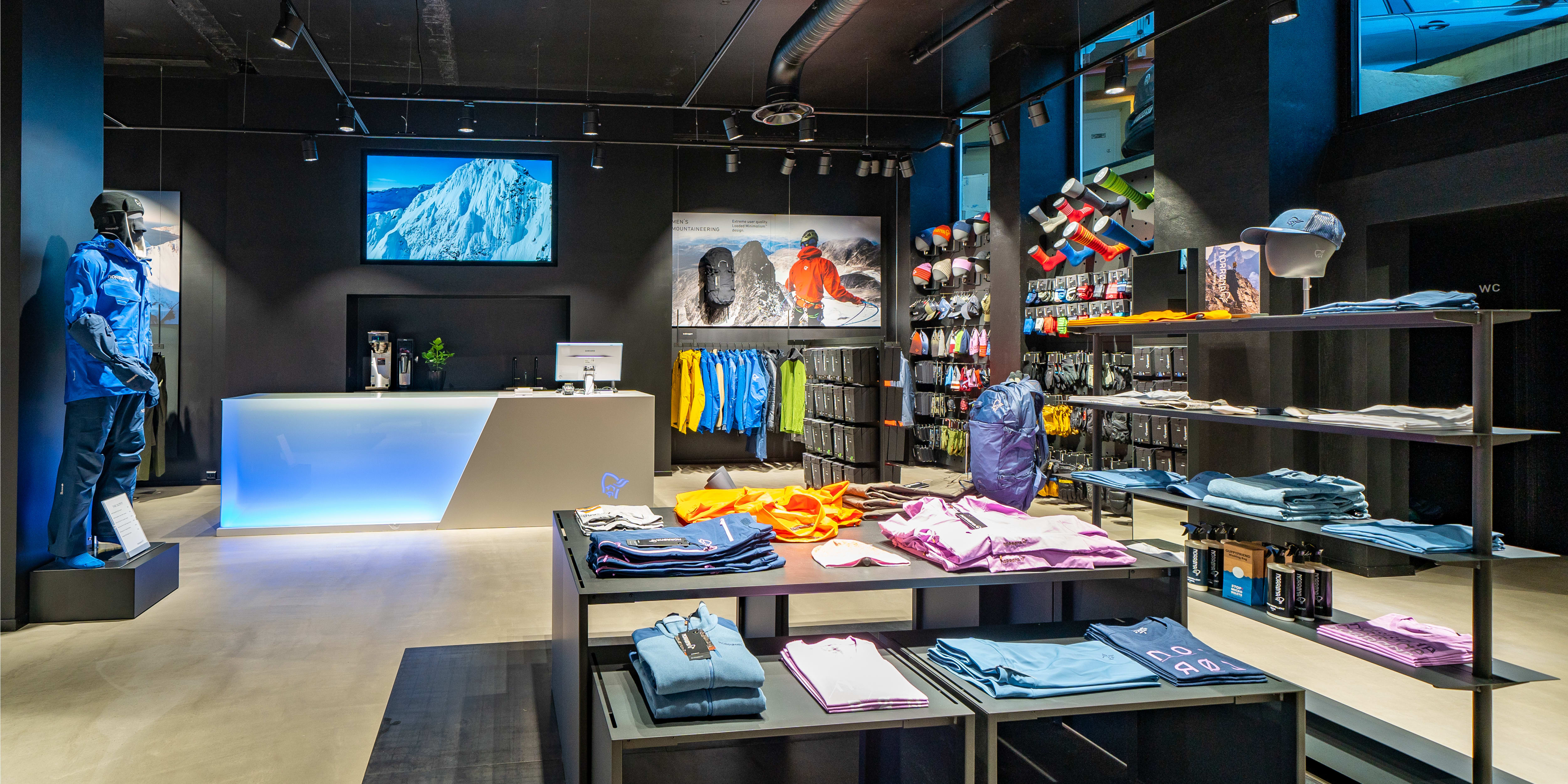 Norrøna store interior featuring displays of outdoor clothing, gear, and a backlit service counter.