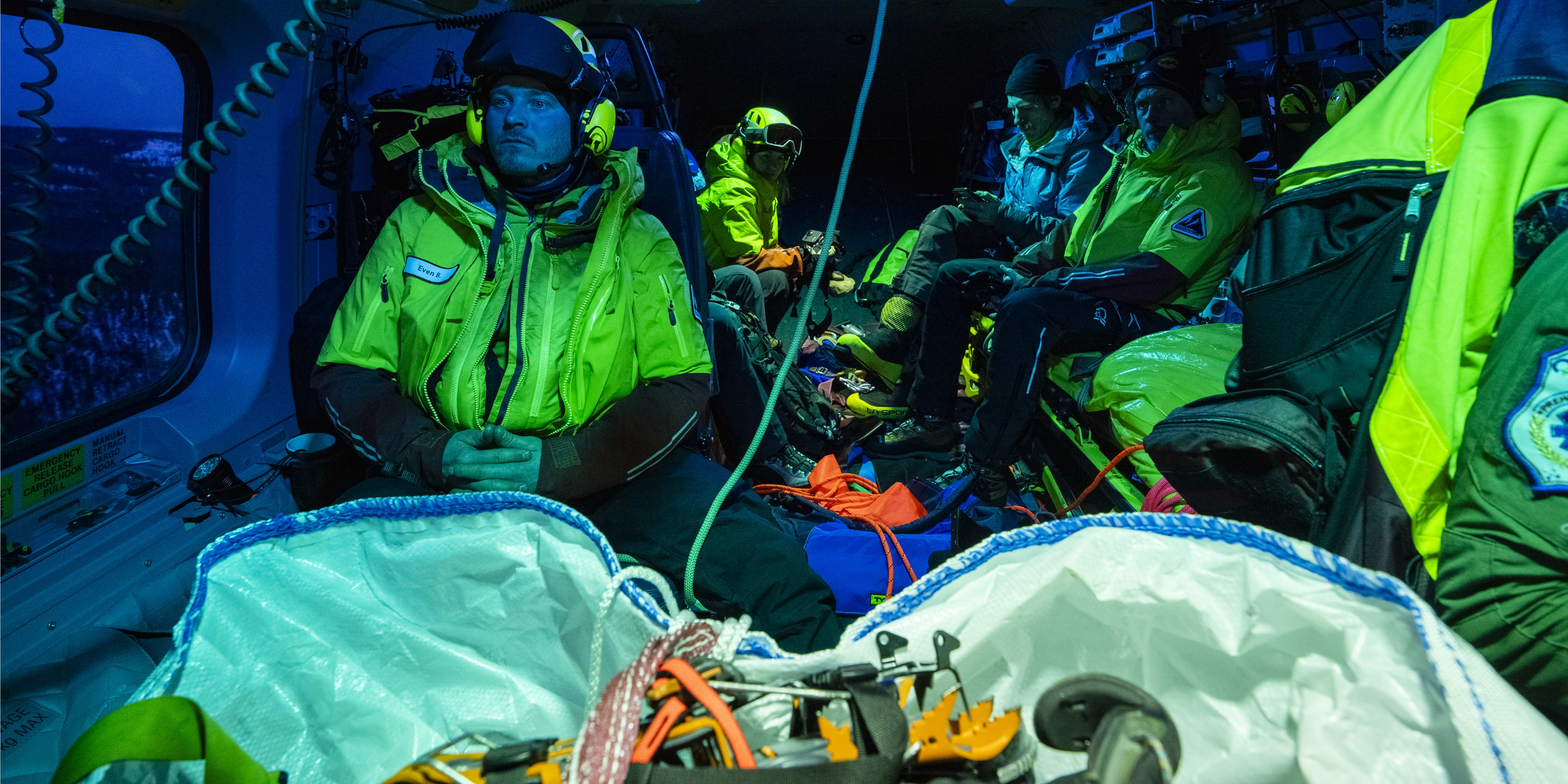 Interior of a helicopter with a Norrøna jacket-wearing man. Rescue equipment and other passengers are also present.  
